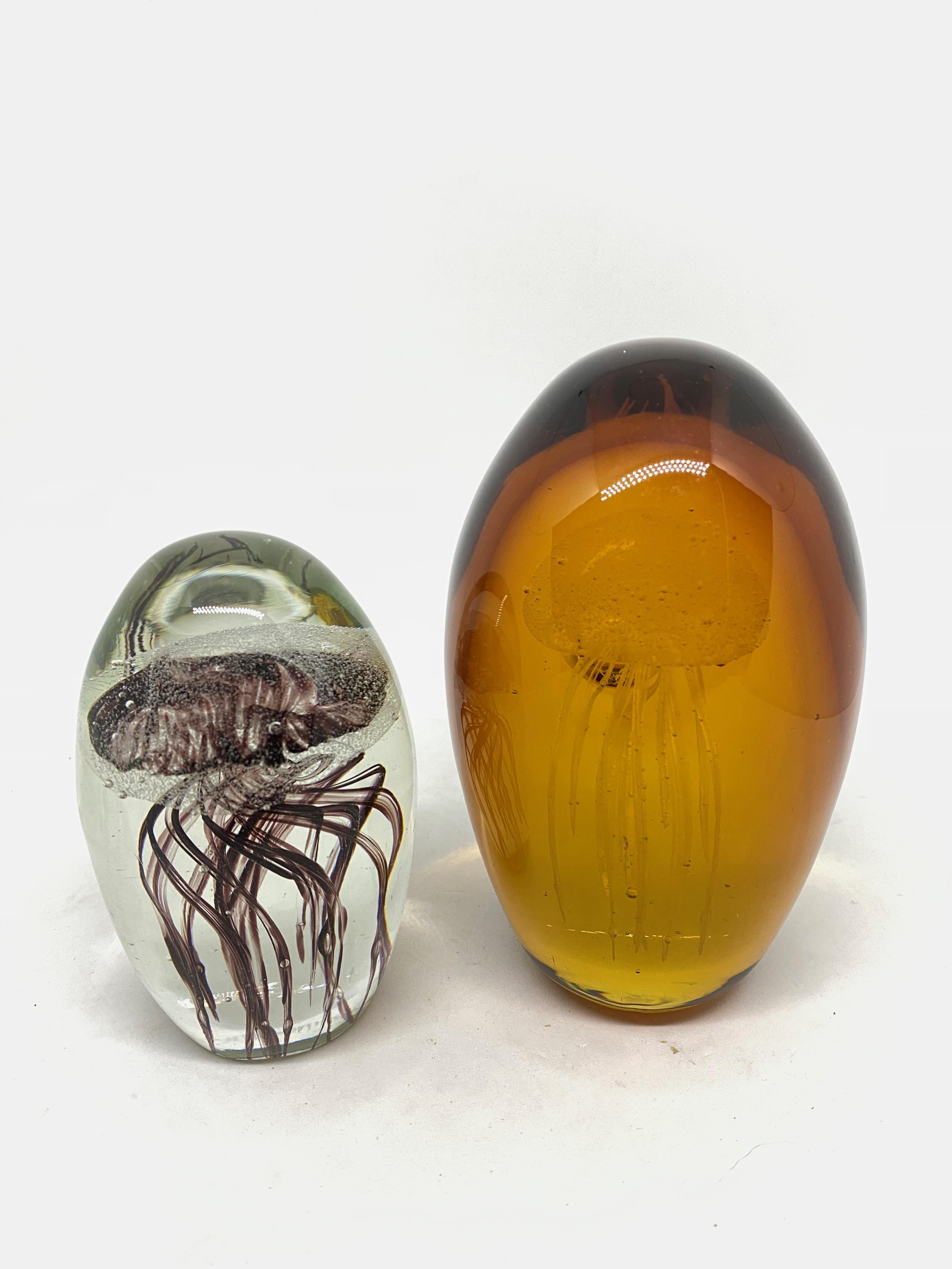 Beautiful set of two Murano hand blown aquarium design Italian art glass paper weights. Showing Jelly Fish inside, in two different colors, floating on controlled bubbles. Colors are a clear glass with purple jelly fish, also an amber glass with