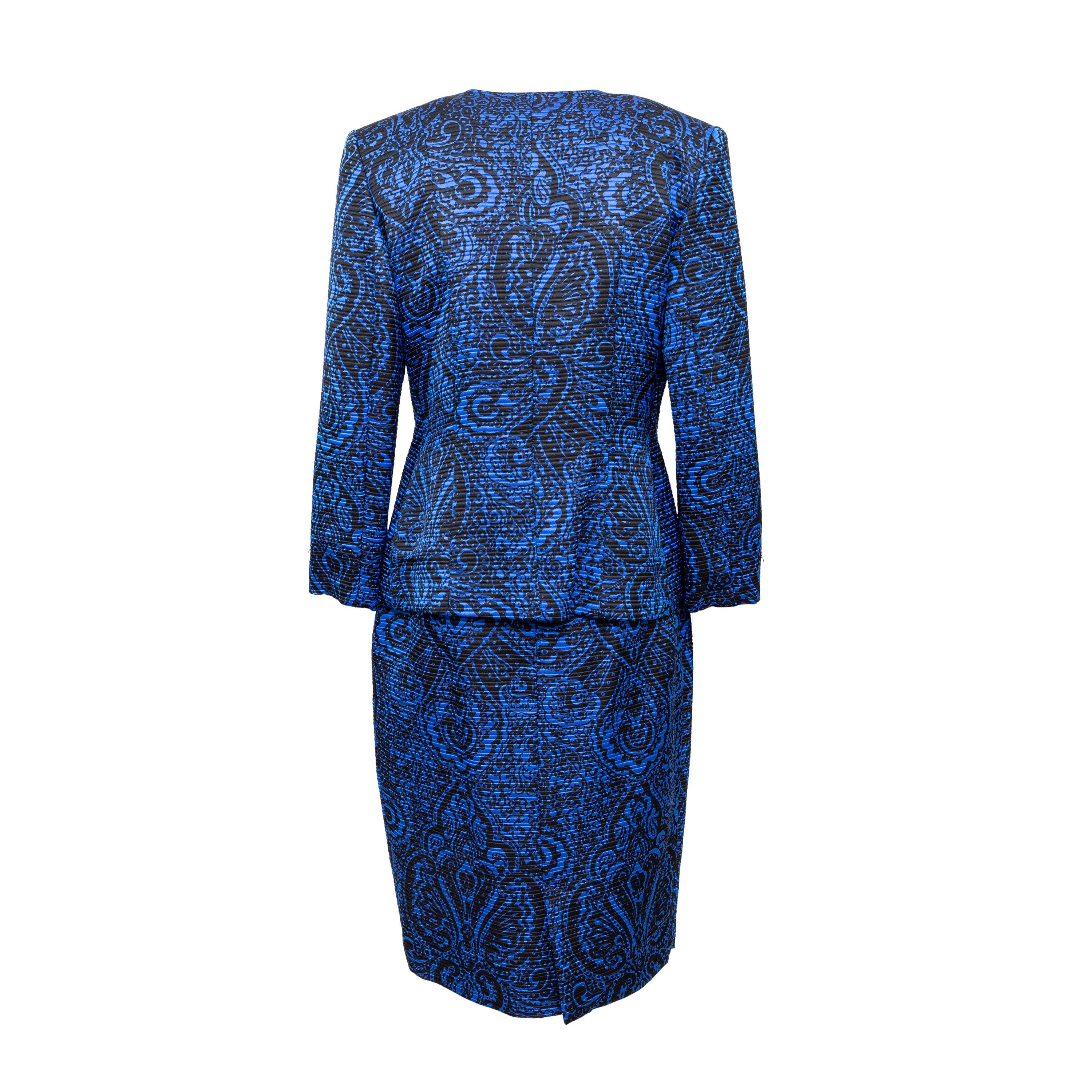 This vintage Jacquard Set in blue with black paisley print features shoulder pads, V-neck with front button closure, and a midi skirt with back closure and vent.
 Remarks: The composition is not listed. There is a hole in the skirt lining. 
