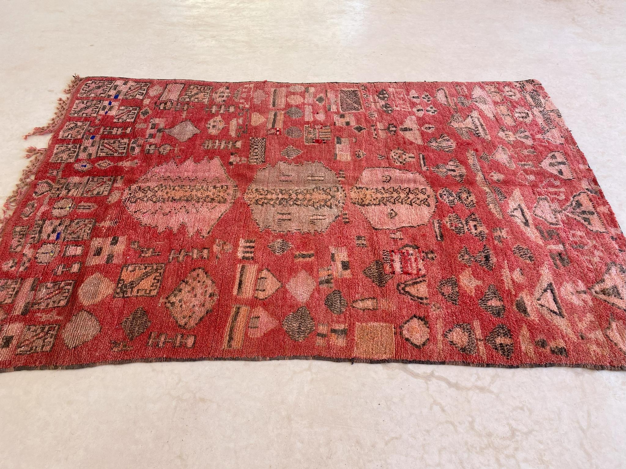 This rug is a collector piece! It is called a Rehamna rug and was probably made in the area around the plains of Marrakech, Morocco.

The background color of this rug is a subtle red with black and pink designs. The rich composition is made of three