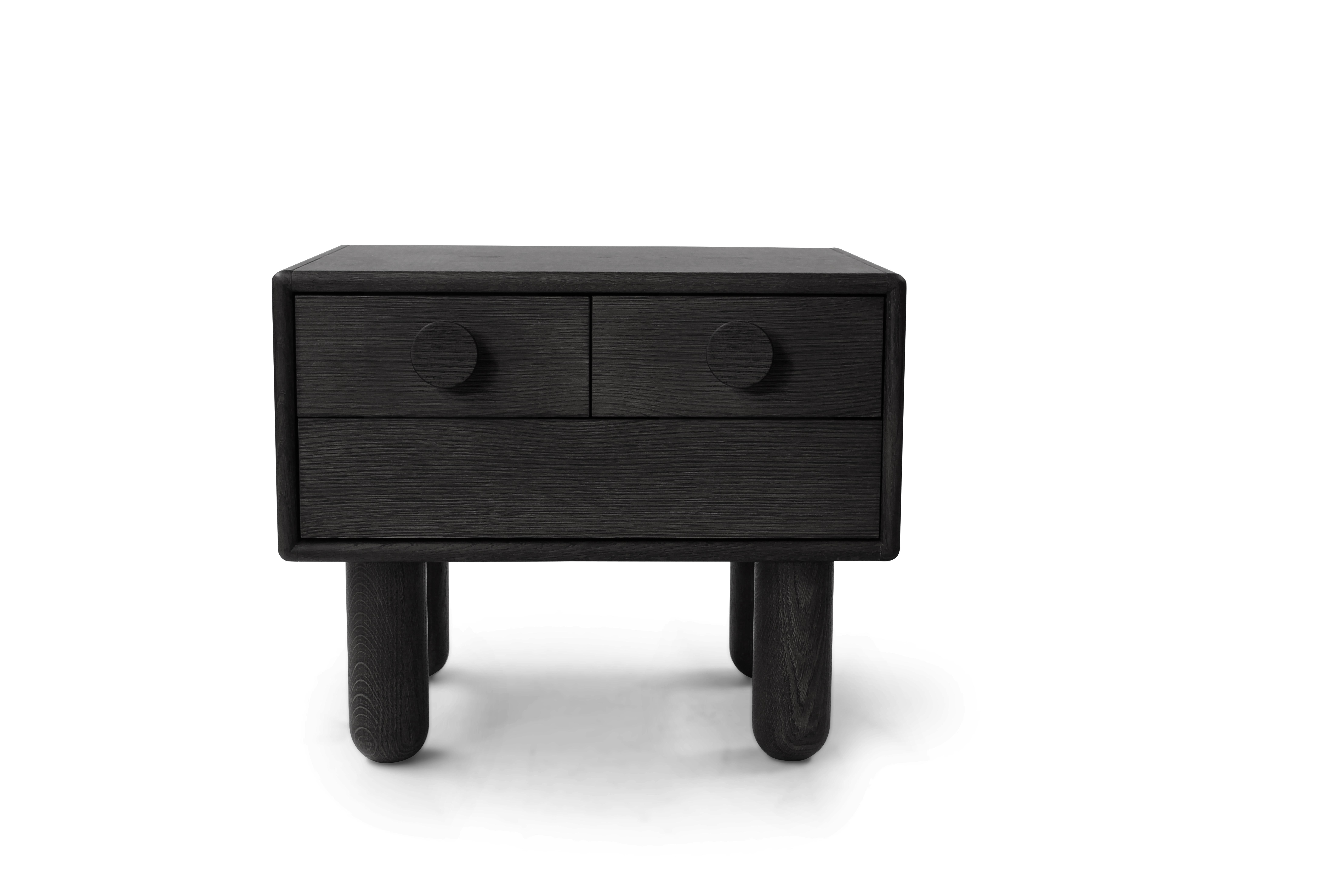 Table de chevet en bois de belle facture, au design minimaliste et aux arêtes douces et arrondies. Il comporte trois tiroirs avec des boutons circulaires en bois, offrant un rangement pratique tout en conservant une esthétique élégante. Soutenue par