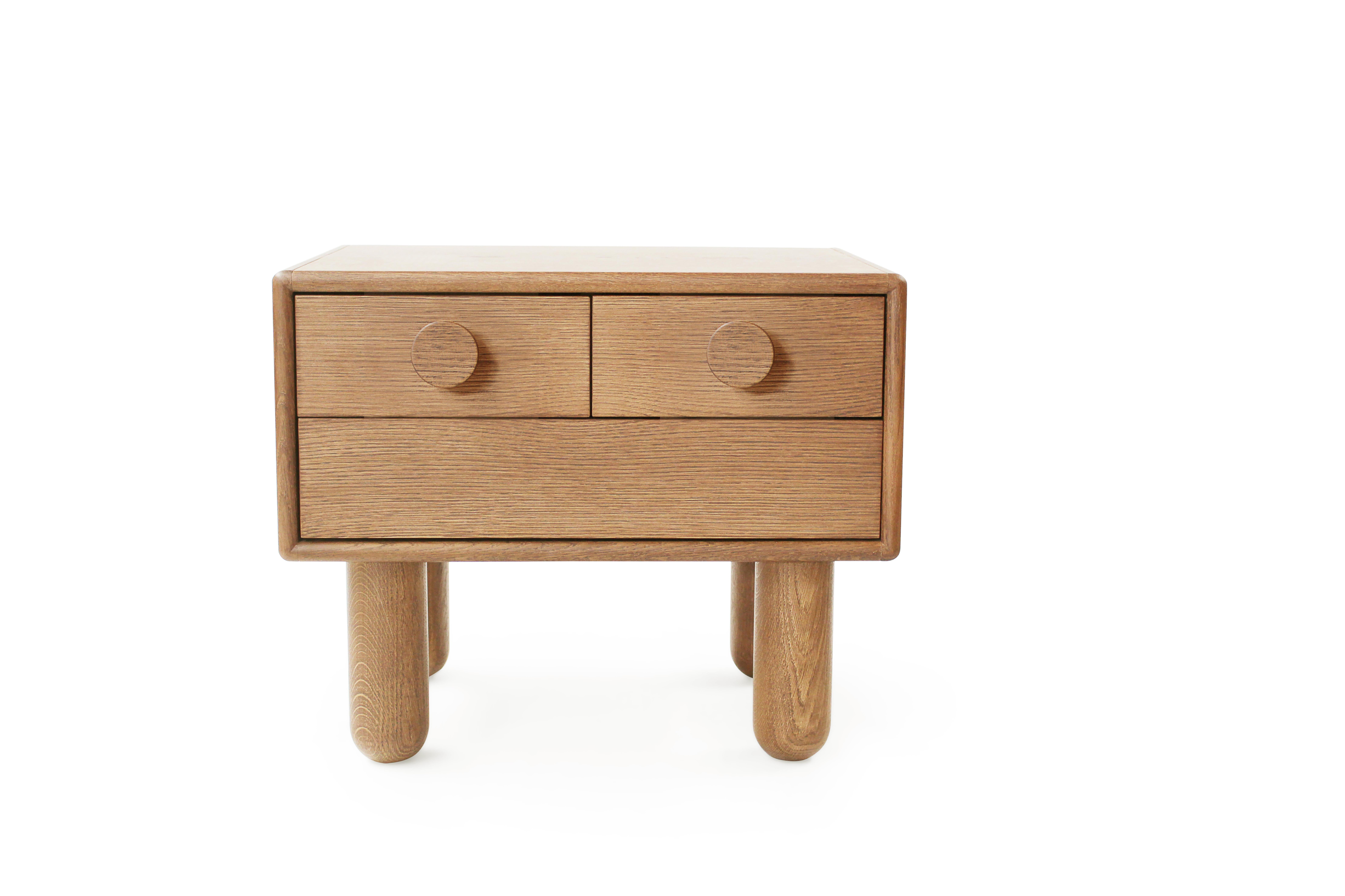 Table de chevet en bois de belle facture, au design minimaliste et aux arêtes douces et arrondies. Il comporte trois tiroirs avec des boutons circulaires en bois, offrant un rangement pratique tout en conservant une esthétique élégante. Soutenue par