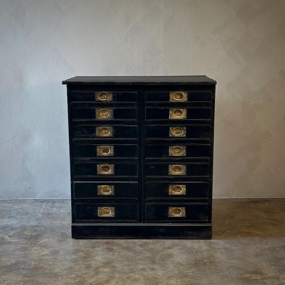 Commode de collection rustique en bois anglais du XIXe siècle, peint en noir, comprenant deux colonnes de sept tiroirs, chacun doté d'une poignée de tirage en laiton. Posée sur un socle, cette pièce peut être utilisée comme armoire, coffre ou petit