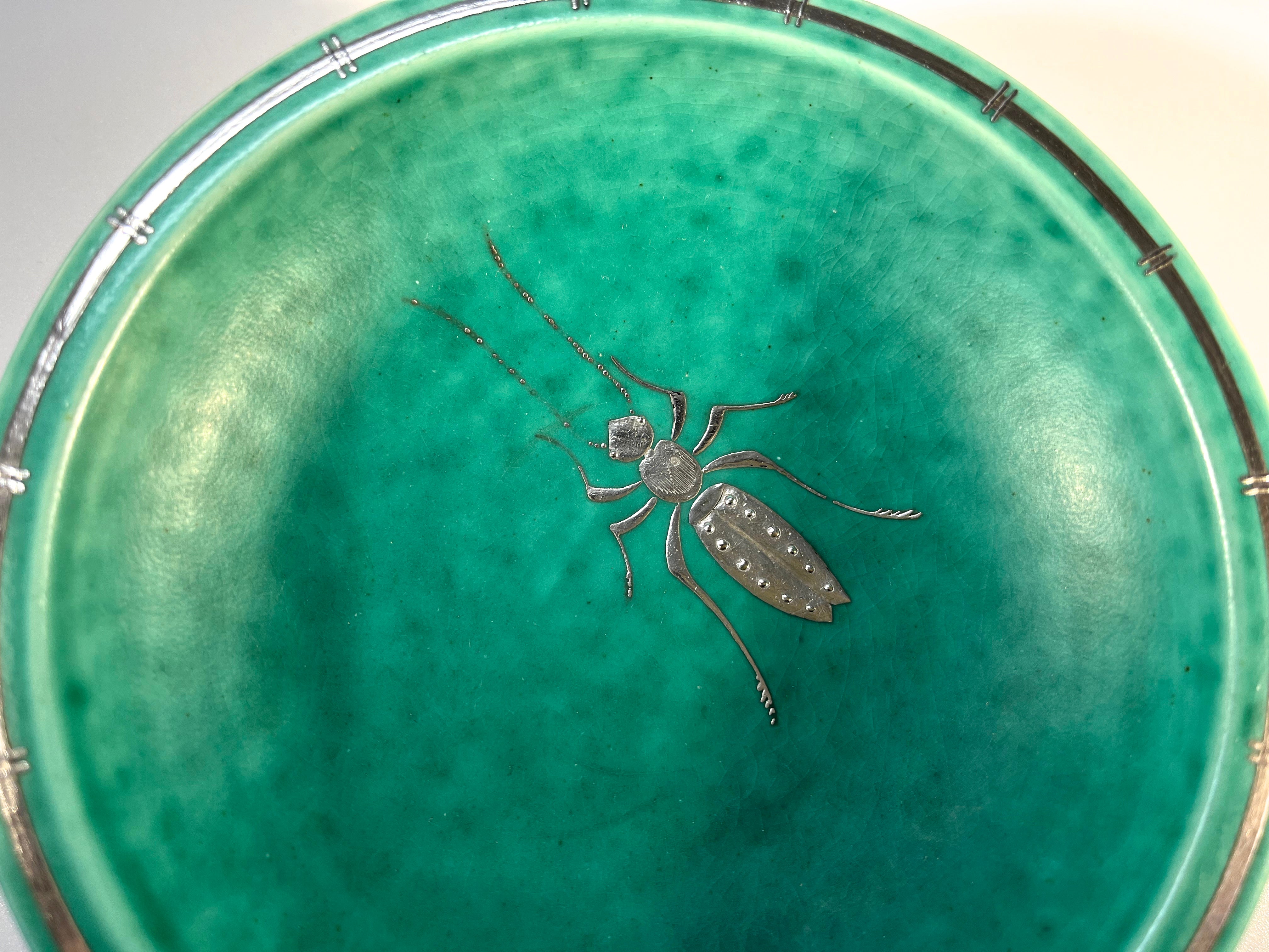 Un grande scarabeo esotico in argento applicato adorna questo insolito pezzo di gres ARGENTA di Wilhelm Kage per Gustavsberg, Svezia. 
Decorazione 