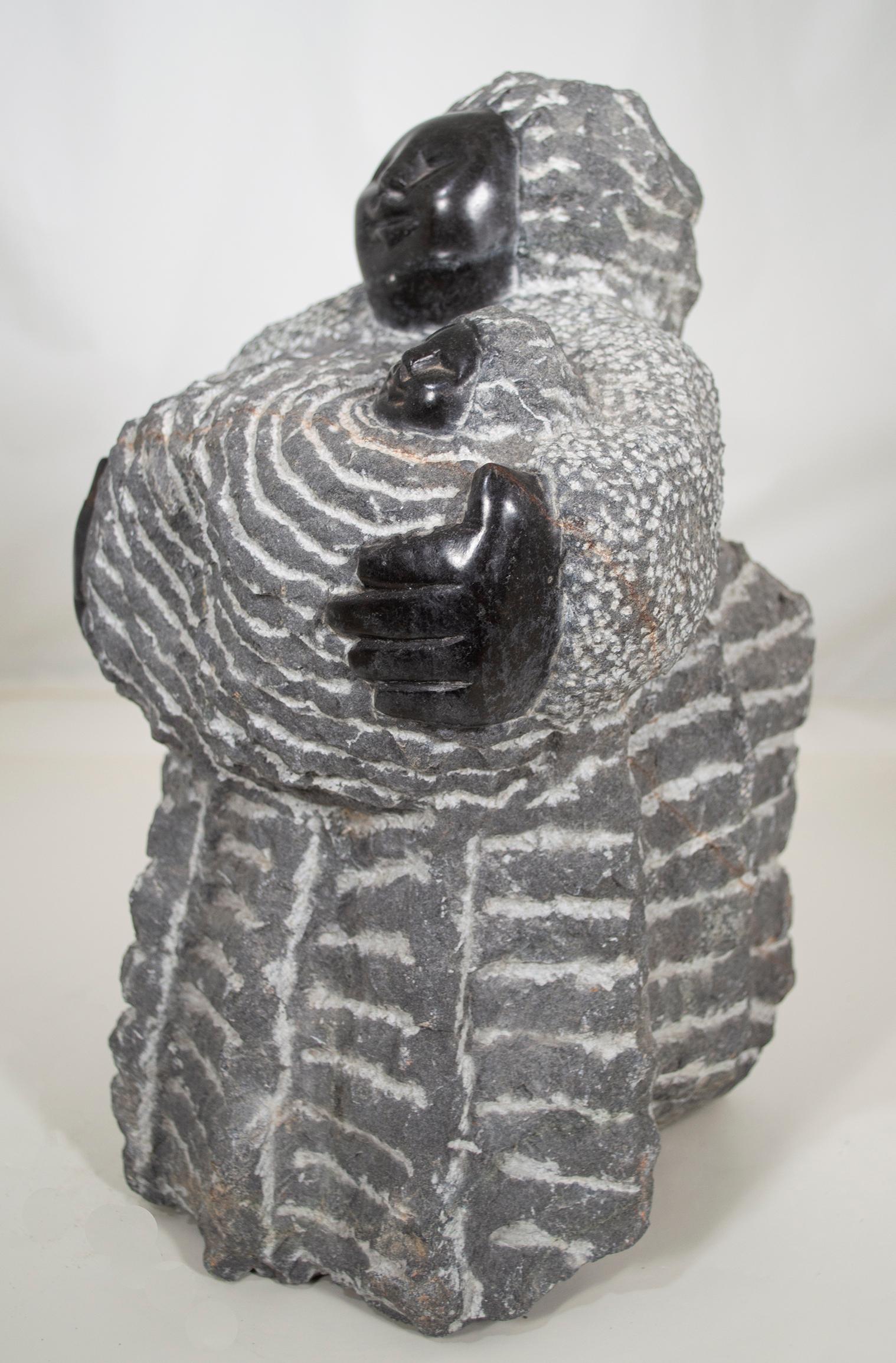 'Grandmother With Her Granddaughter' is an original black serpentine sculpture by the celebrated second generation Shona artist Colleen Madamombe. The sculpture presents a character common to Madamombe's work: a woman with a round face and wearing a