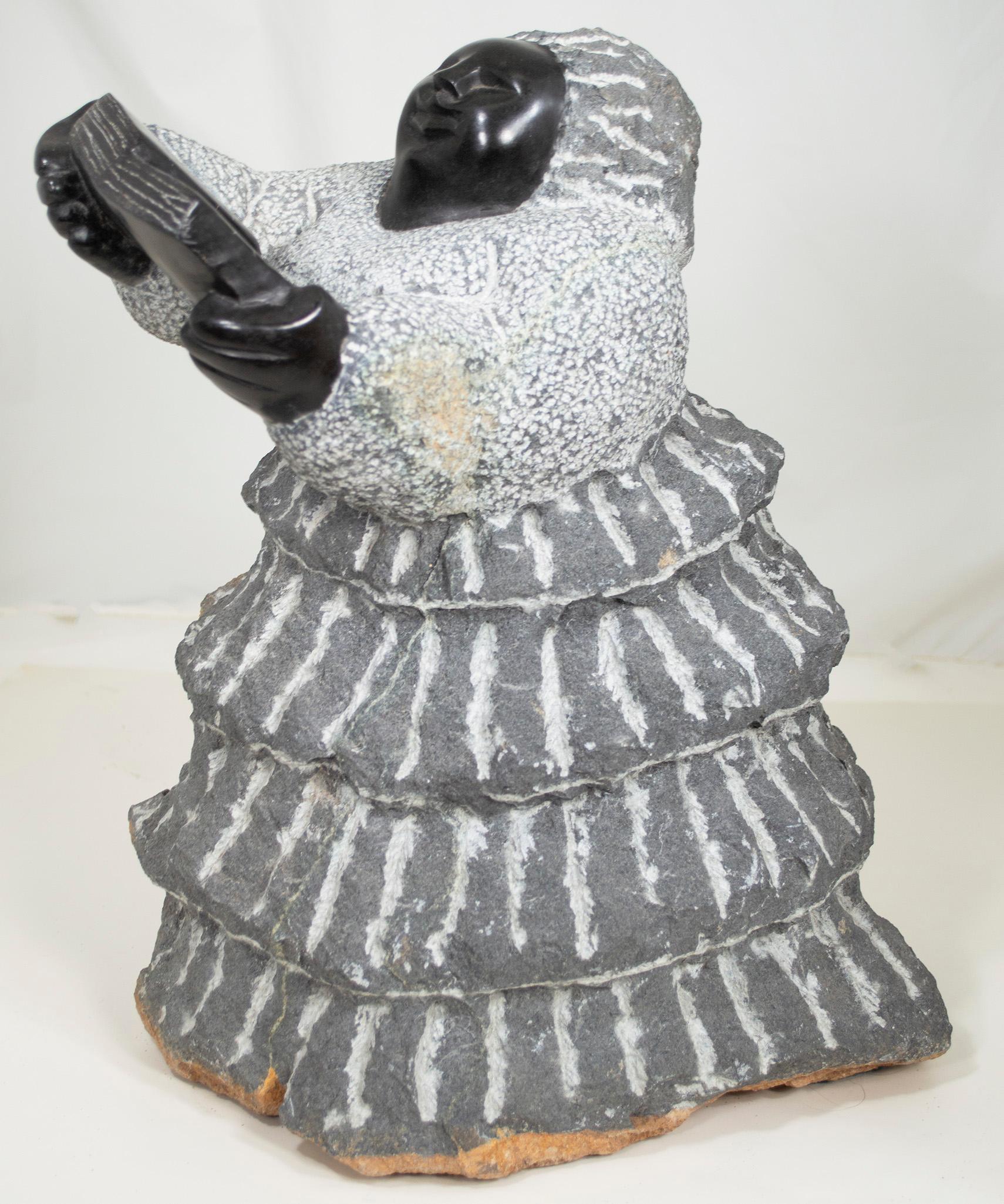 Teacher or Preacher" est une sculpture originale en serpentine noire réalisée par Colleen Madamombe, célèbre artiste shona de la deuxième génération. La sculpture présente un personnage commun à l'œuvre de Madamombe : une femme au visage rond, vêtue