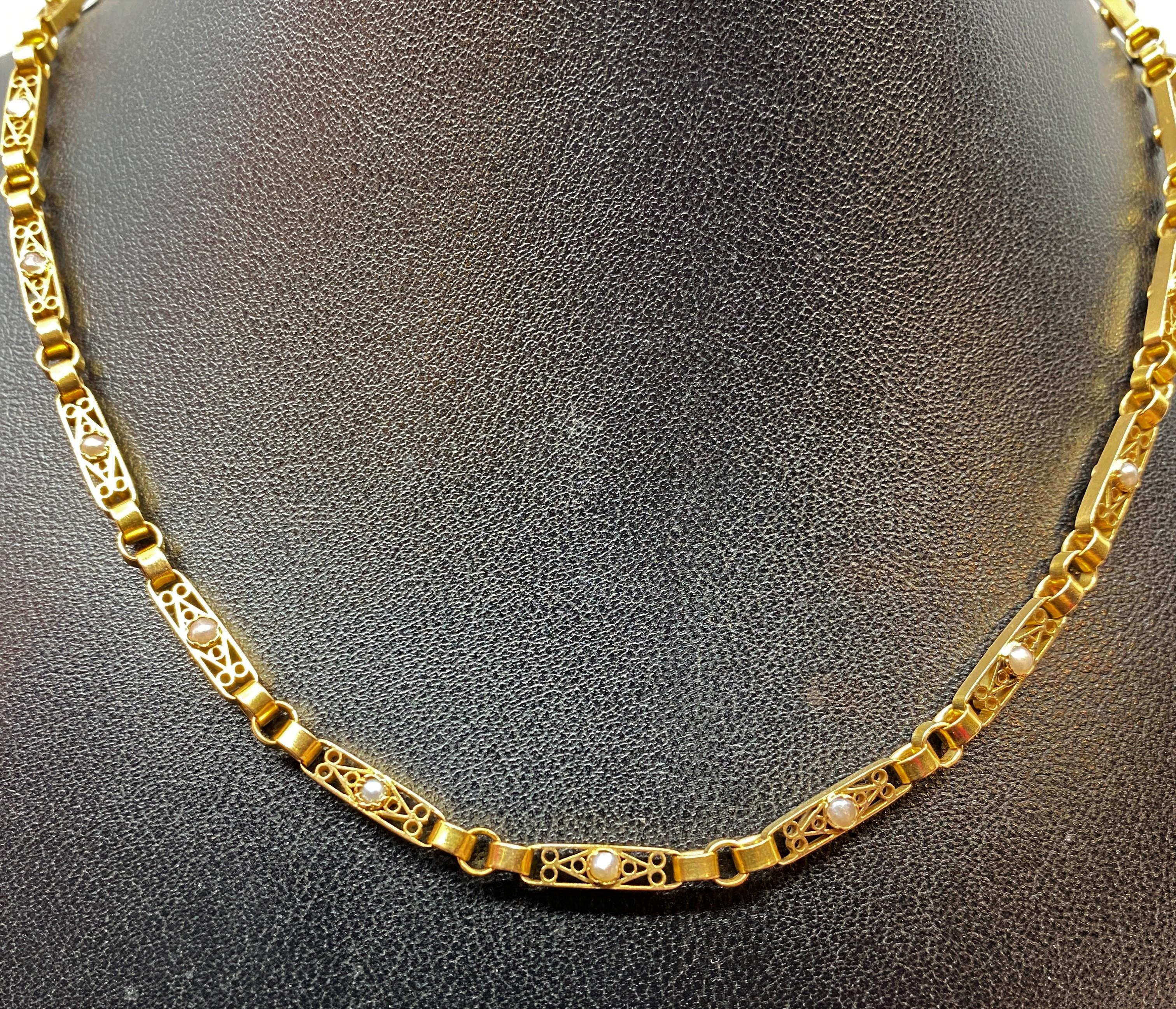 Charmant collier en or 18 carats formé de 16 maillons rectangulaires double face, sertis d’une demi perle fine dans un décor ajouré de filigranes. Ils sont reliés entre eux par trois anneaux ronds retenus jusqu’au fermoir par des mailles forçat. Le