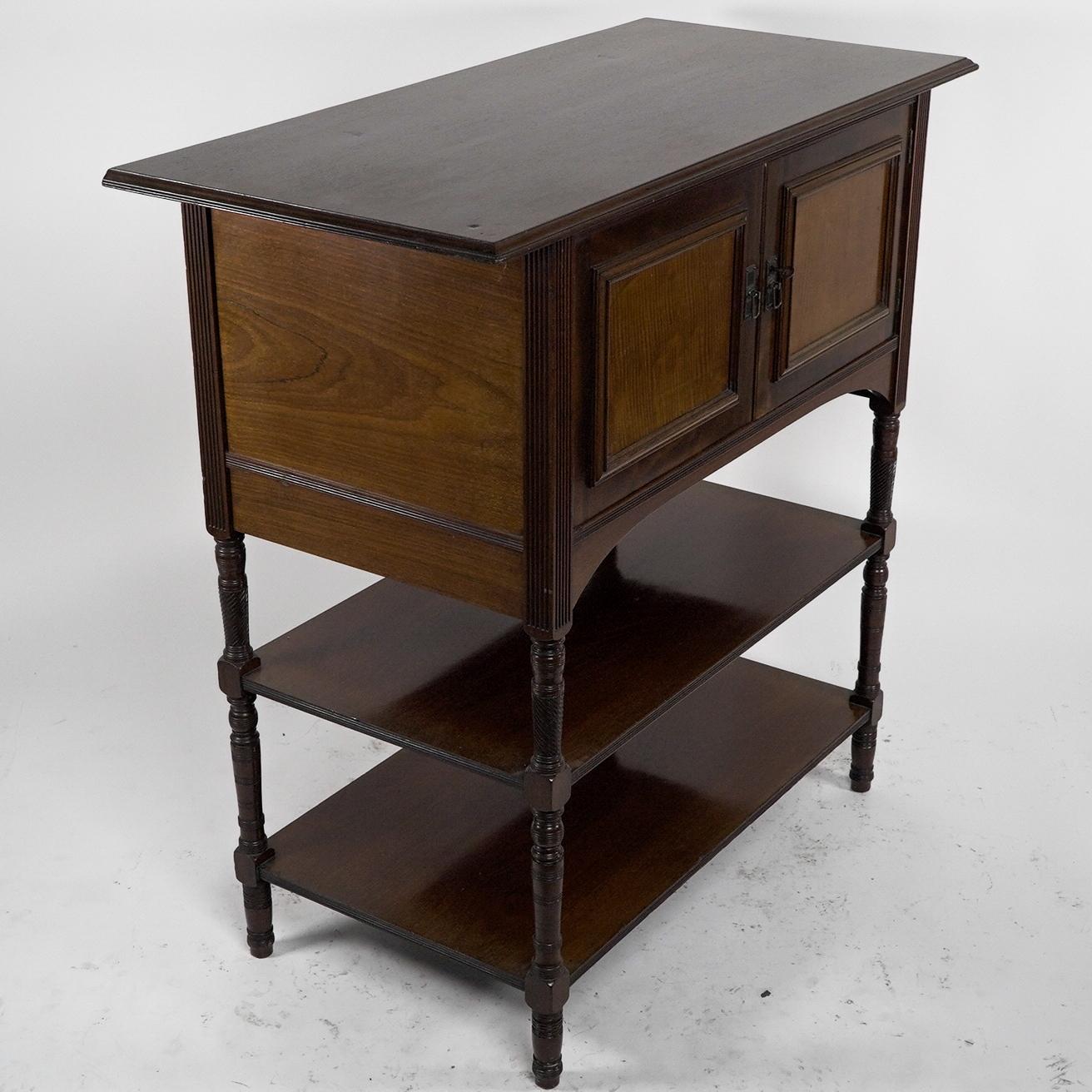Collinson and Lock EW Godwin attributed. An Aesthetic Movement Mahogany side cabinet, the upper cupboard doors with contrasting fruit wood panels and little Japanese style brass handles. Two flat open shelves to the lower section united by finely