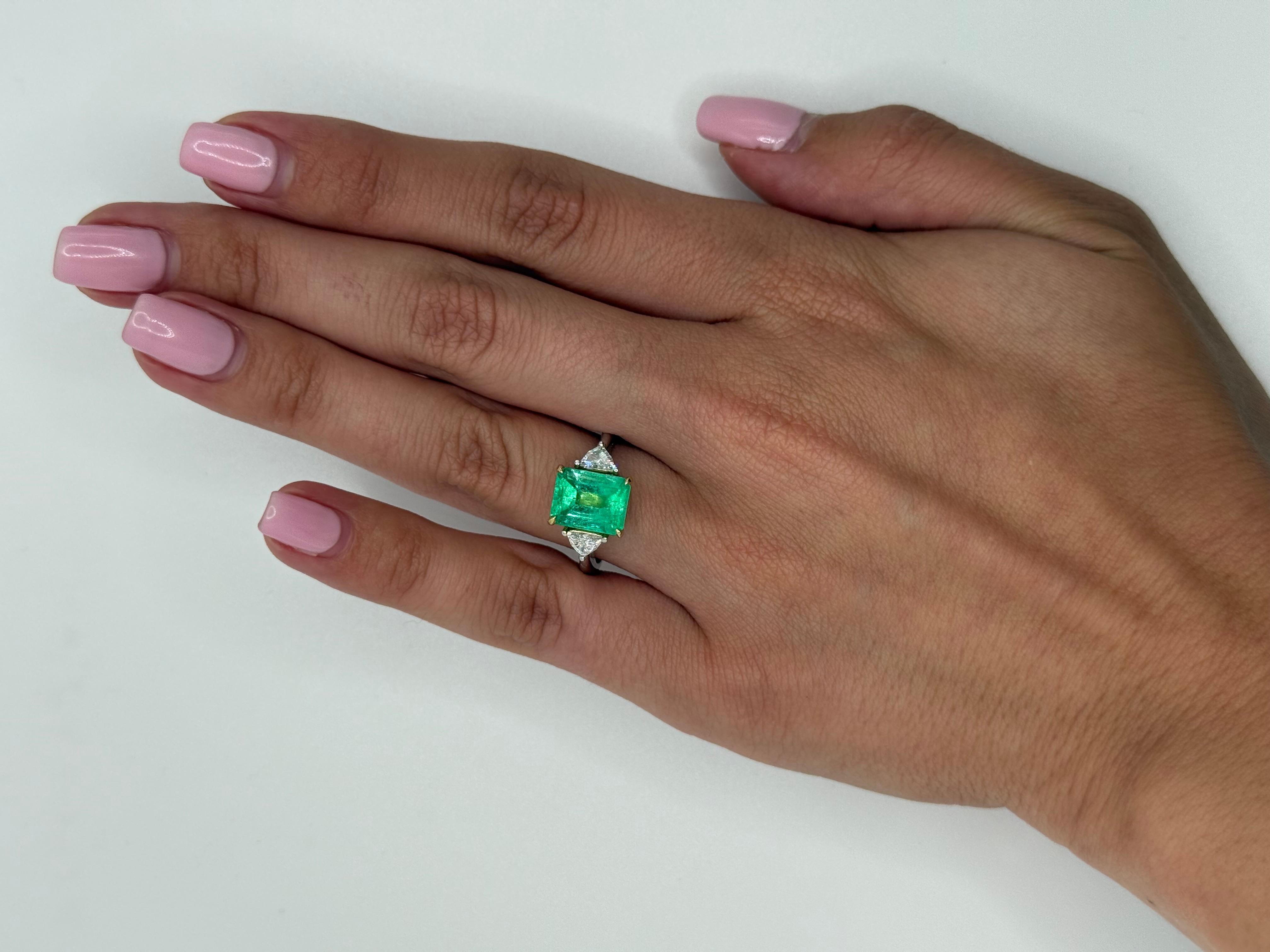 Cette bague remarquable met en valeur une émeraude de 3,20 carats, admirée pour sa teinte vibrante vert pistache, une couleur qui apporte à la fois fraîcheur et chaleur à la pièce. La pierre centrale est flanquée de deux diamants taille trillion,