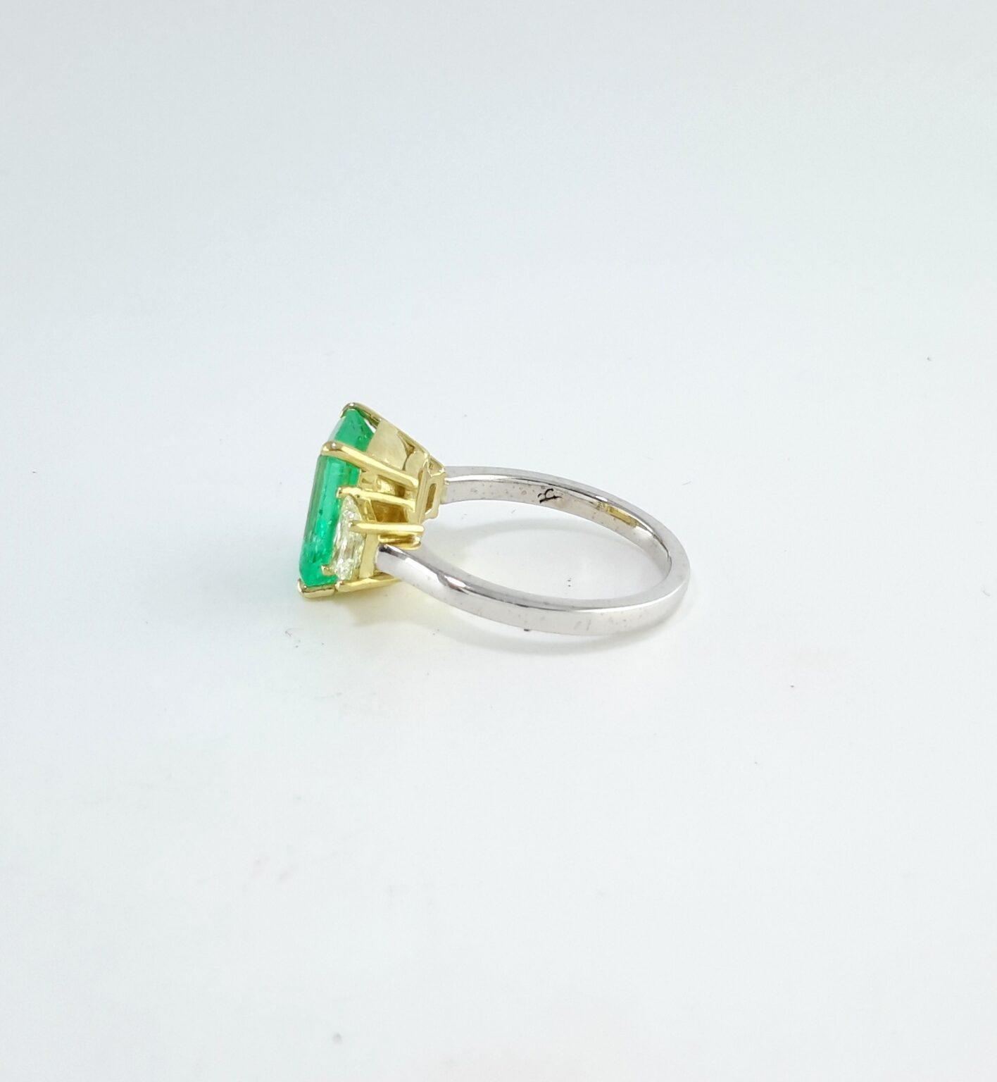 Elegant and full of fresh charm, this three-stone ring features a 3.24 carat Colombian emerald with a rare and vibrant light green hue—reminiscent of a soft pistachio tone. The emerald is emerald-cut, showcasing clean lines and a beautifully open