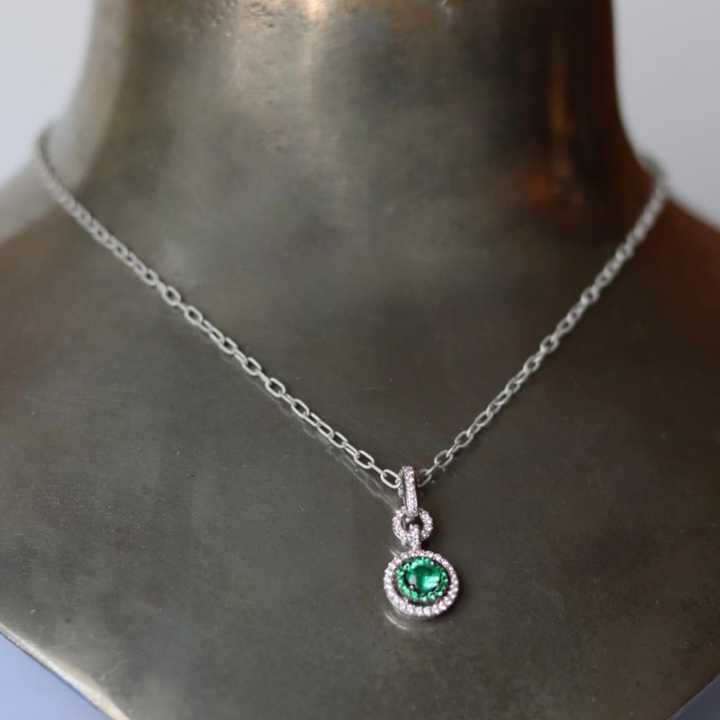 This Charm pendant is handmade in Belgium the traditional way, by jewelry artist Joke Quick,  ( no casting or printing envolved) in 18K white gold and is hand set with a Colombian Emerald centerstone and a Colombian Emerald and White Diamond Halo.