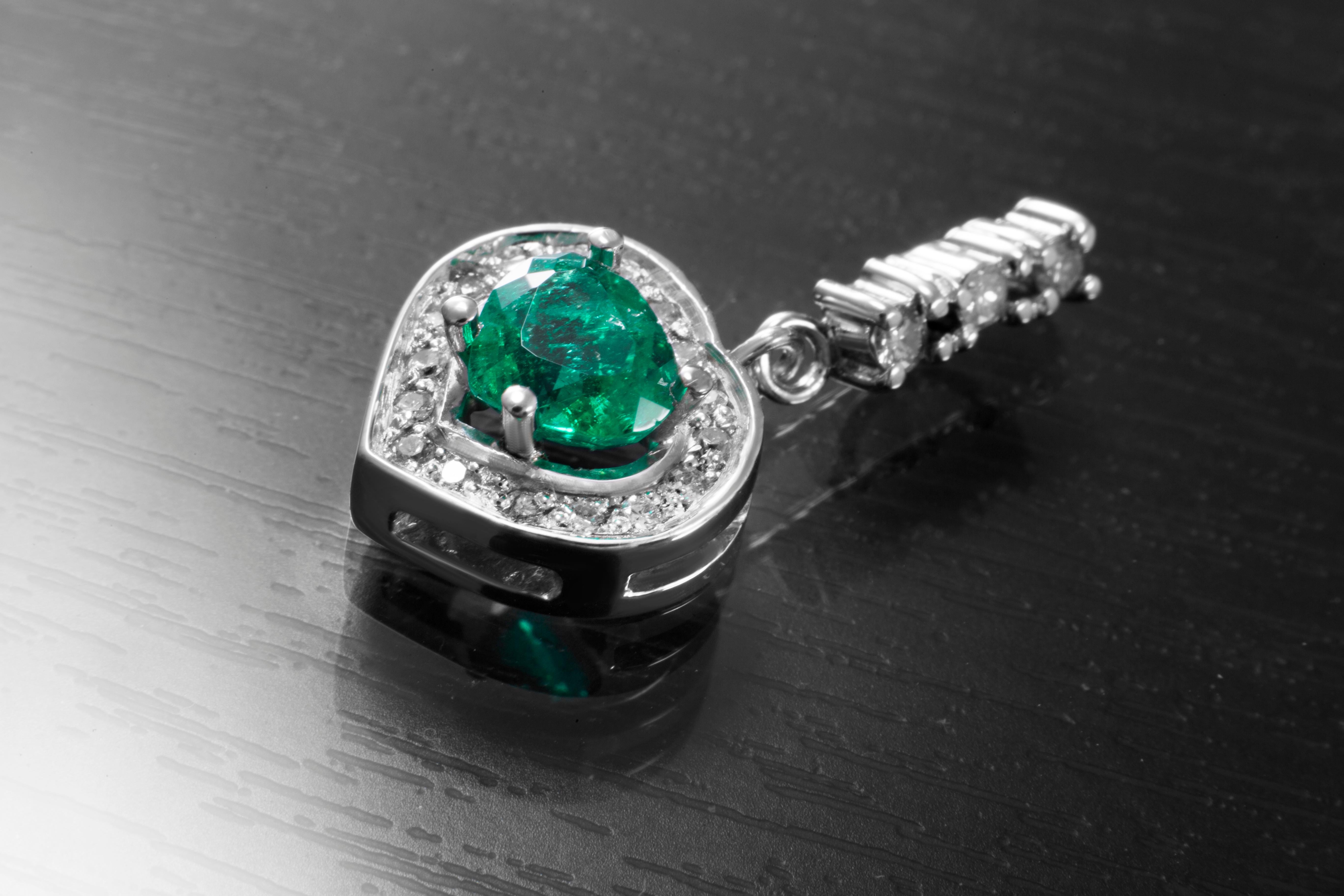 A pendant consisting of a 0.9 carat certified F3 quality Colombian Muzo emerald set in 18 carat white gold with a diamond melee, comprising 3 larger stones, of 0.09 carats, I-J colour and 17 smaller diamonds, totalling 0.17 carats, I-J