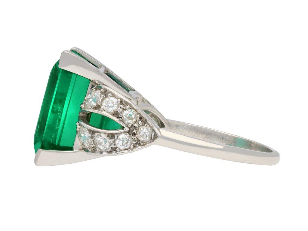 Colombian emerald and diamond ring. Set to centre with a rectangular emerald-cut natural Colombian emerald with minor clarity enhancement in an open back claw setting with an approximate weight of 14.00 carats, flanked by fourteen cushion shape old