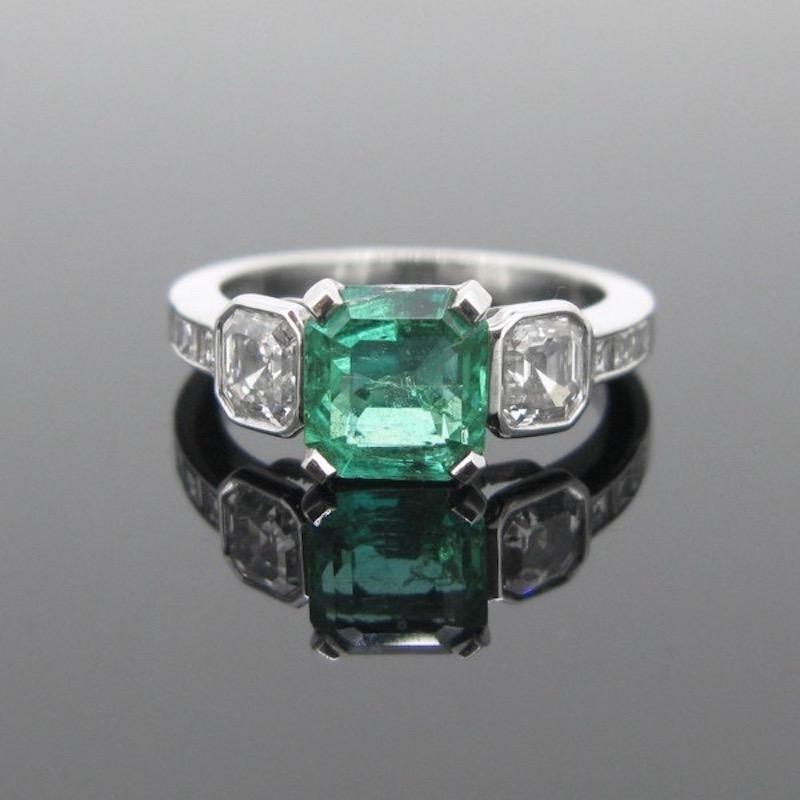 This ring is fully made in platinum. It is set in its centre with a beautiful bluish green emerald from Colombia weighing around 1.30ct. It is shouldered with Asscher and princess cut diamonds. The ring has been controlled with the UK hallmarks for