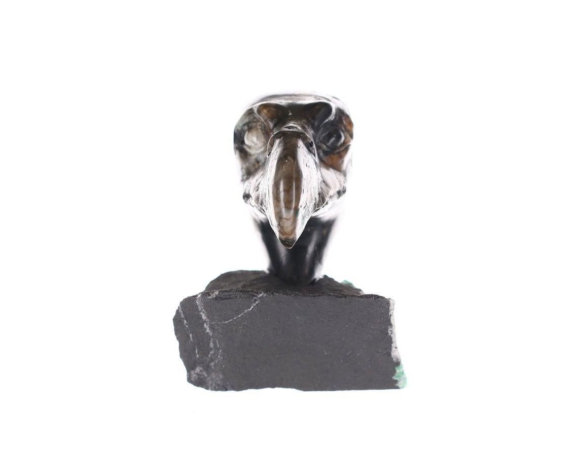 This is a beautiful and one-of-a-kind rough Colombian emerald sculpture. Our national bird, the bald eagle. This majestic head sculpture contains medium-dark, rough Colombian emerald, black shale, and white calcite. The head is beautifully hand