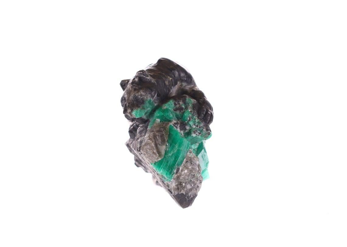 This is a beautiful and one-of-a-kind rough Colombian emerald sculpture. Featuring a rare and exotic, hand-carved Jaguar but made of a mixture of black and gray shale. It is plotting for it's next prey, as it tries to hide behind a rock of calcite