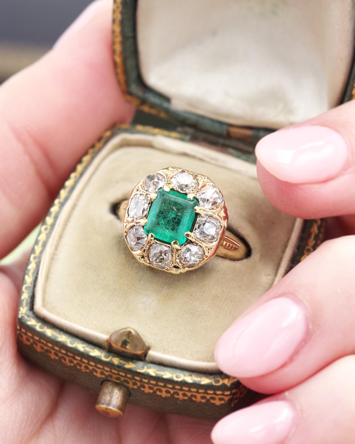 Kolumbianischer Smaragd-Cluster-Ring in 18k Gold. Ring aus der Belle Epoque, besetzt mit einem rechteckigen kolumbianischen Smaragd mit geschliffenen Seiten von 0,81 Karat. Der Smaragd ist von acht Diamanten im Altschliff (je 0,12ct) umgeben.