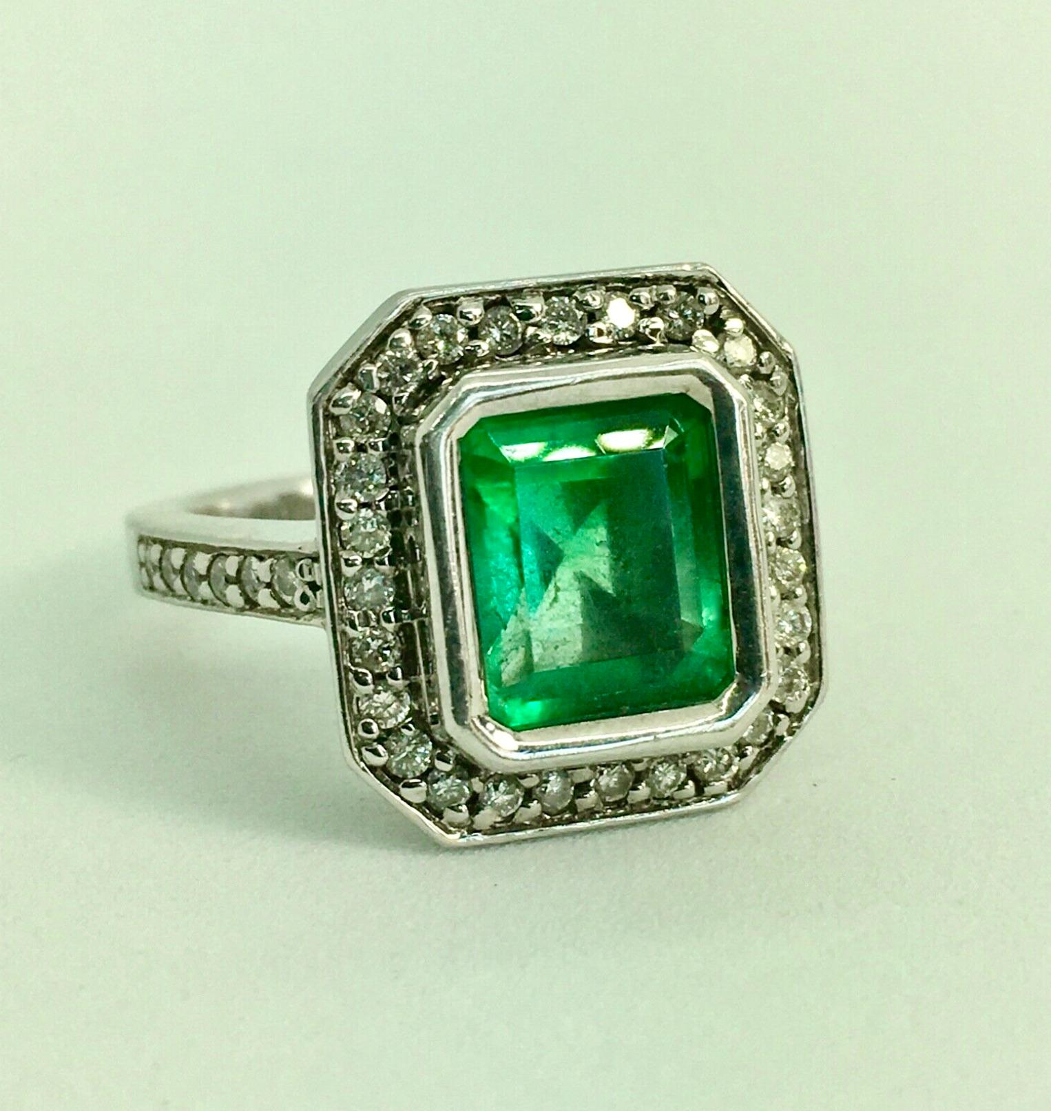 This elegant Art Deco style engagement style ring features a 3.50-carat Colombian emerald emerald cut displaying a vibrant green color. It is accented by a shimmering halo of white round brilliant cut diamonds as well as half way sparkling diamonds