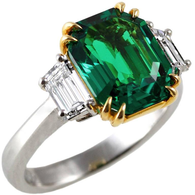 An exceptional three carat emerald-cut Muzo Colombian Emerald, set with two trapezoid diamonds with an estimated color-clarity of F-VS. The emerald exhibits superior color and clarity along with a certificate from AGL stating the origin as Classic