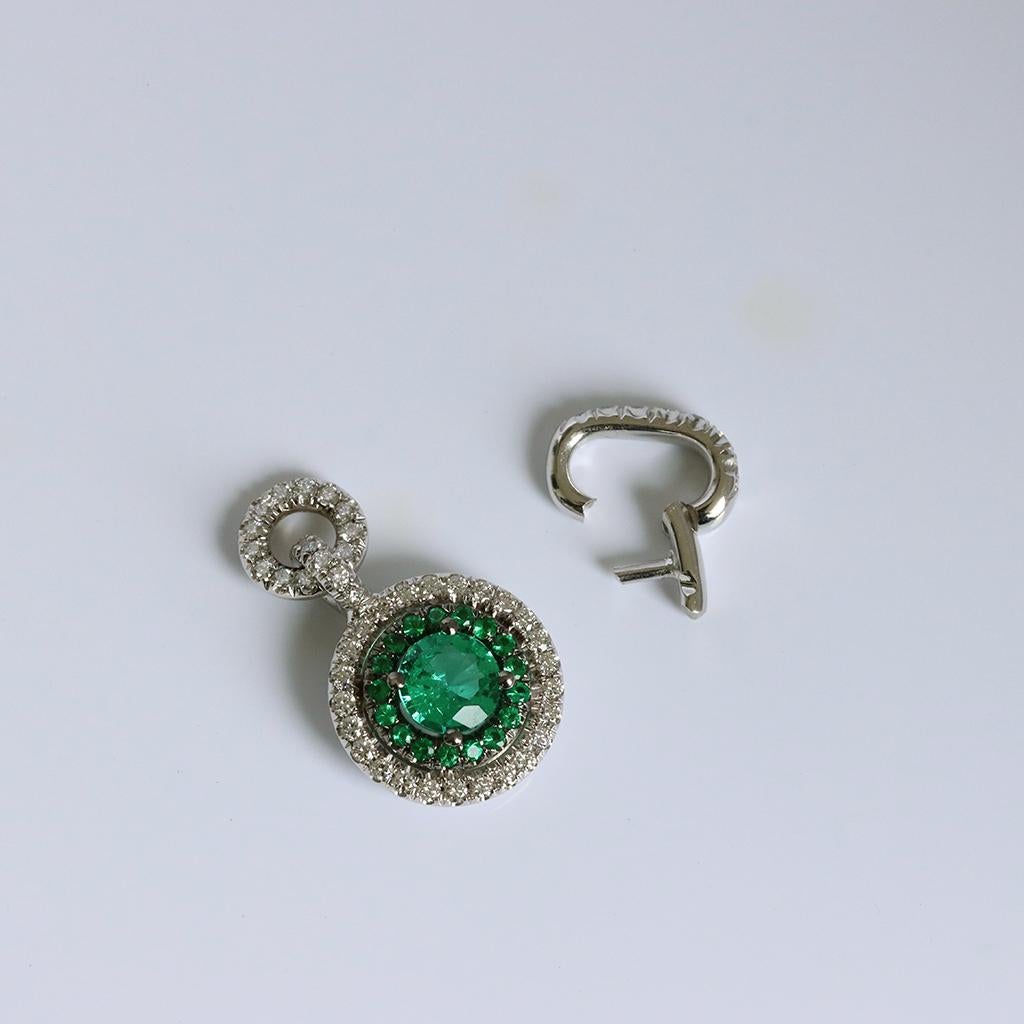 This Charm pendant is handmade in Belgium the traditional way, with no casting or printing involved, by jewelry artist Joke Quick, in 18K white gold and is hand set with a Colombian Emerald centerstone and a Colombian Emerald and White Diamond Halo.