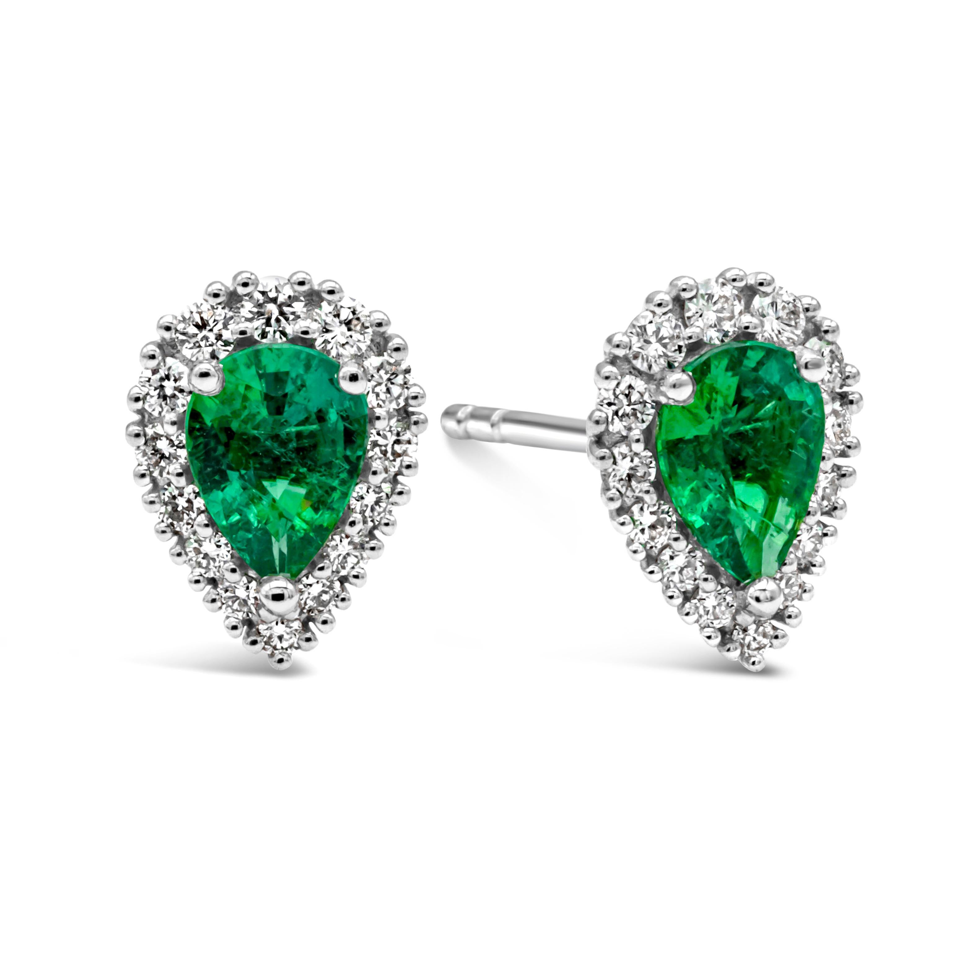 A simple and classic pair of stud earrings showcasing a pear shape Colombian green emerald weighing 0.63 carats total, set in a classic three prong setting. Surrounded by a single row of brilliant round shape diamond weighing 0.26 carats total, G