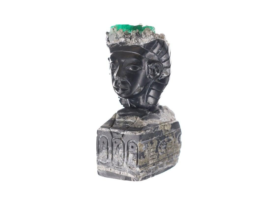 This is a beautiful and one-of-a-kind rough Colombian emerald sculpture. It is an Egyptian-styled rough; handcrafted, and made of natural black and gray shale with minimal traces of pyrite along the edges. The Colombian emerald rough sits at the top