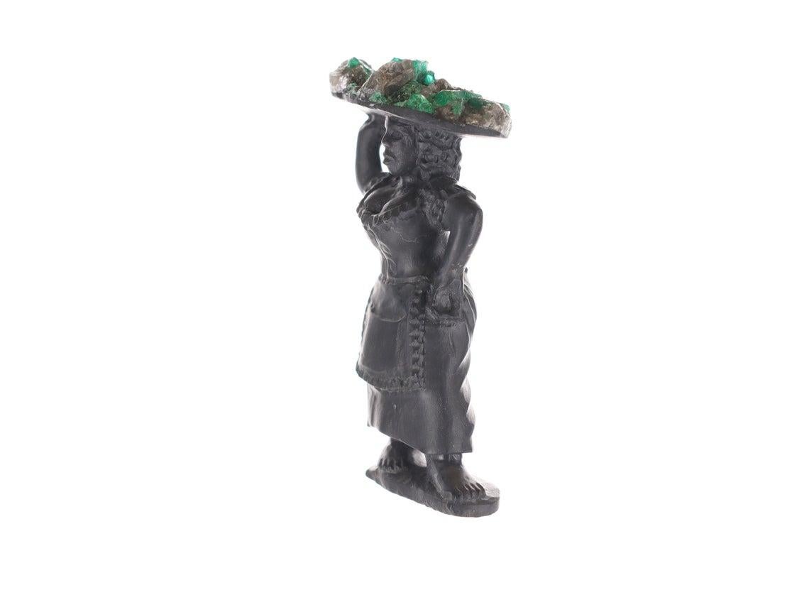 This is a beautiful and one-of-a-kind rough Colombian emerald sculpture. This unique item represents the woman in the morning, selling fruit to their local hometowns in Colombia. In this case, she carries a tray holding natural Colombian emerald