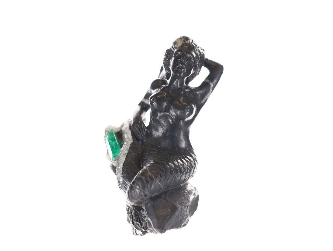 Il s'agit d'une magnifique sculpture d'émeraude colombienne brute, unique en son genre. Il présente une magnifique sirène sculptée à la main dans du schiste noir et gris, avec des détails complexes, des écailles de sa queue aux mains dans ses