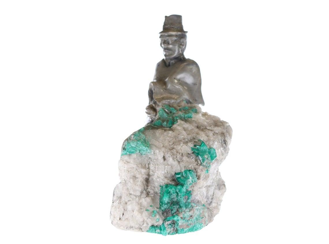 This is a beautiful and one-of-a-kind rough Colombian emerald sculpture. This piece signifies does not just a man kneeling down, but a true Colombian camper. These Colombian campers date back many decades, making a living by working hard day by day.