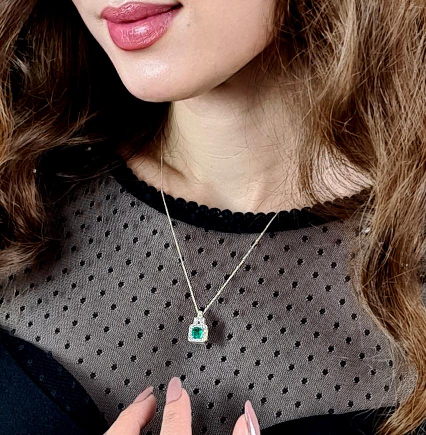 A rectangular shaped emerald in beautiful vivid green colour surrounded by a glimmering border of glistening white round brilliant diamonds. The layout of the pendant in entirety resembles a building as towering on top of the emerald are smaller and