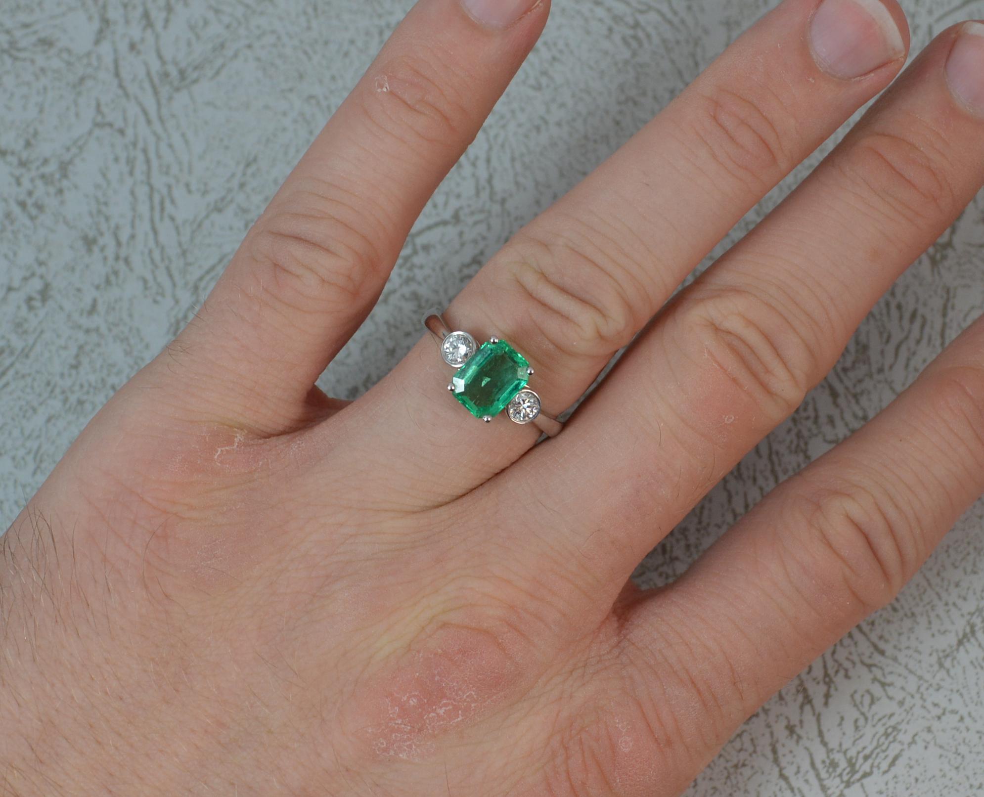 A superb Emerald and Diamond three stone ring.
Modelled in 18 carat white gold throughout.
Designed with a emerald cut emerald to centre in four claw setting. Believed to be Colombian origin. 6.3mm x 8.2mm approx. To each side is a 0.2 carat round