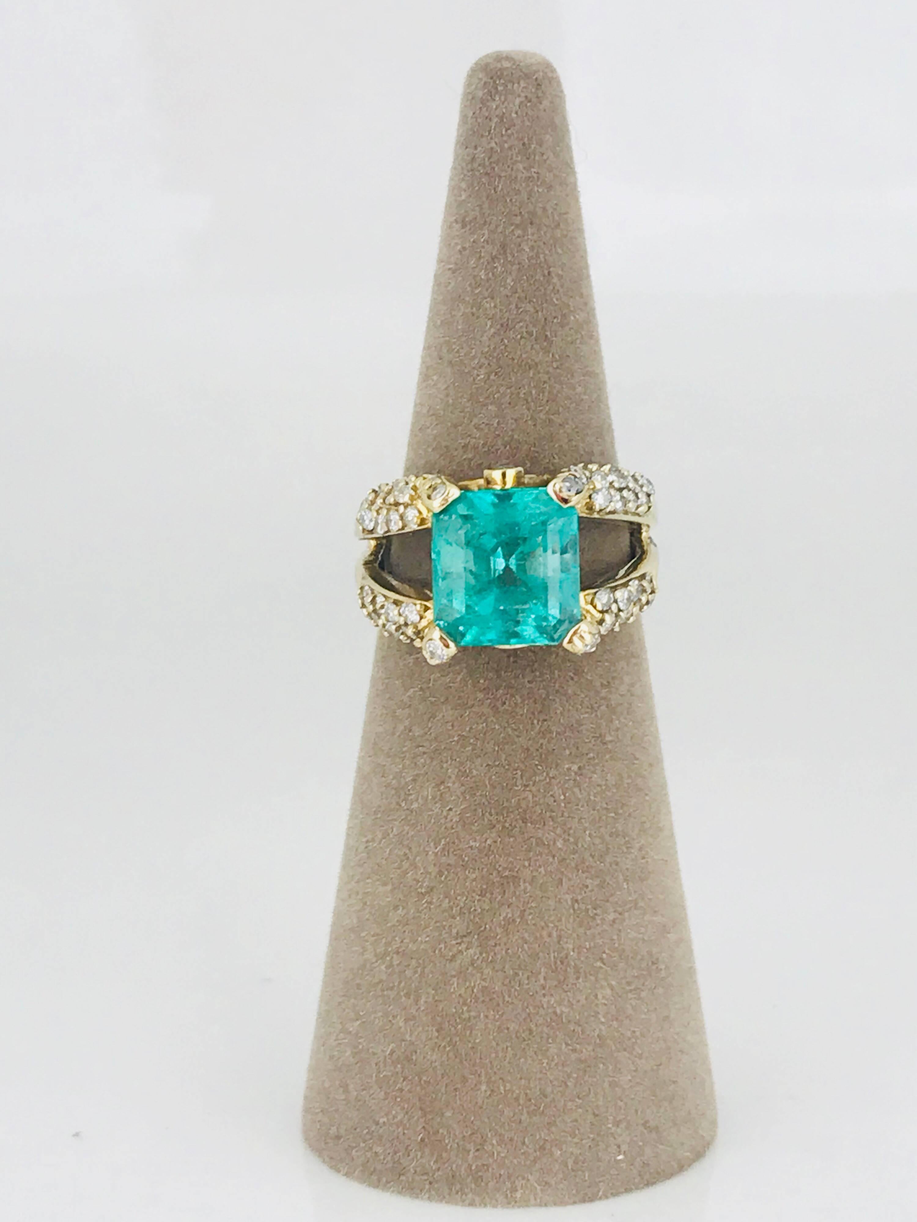 Contemporary designed 14 karat yellow gold ring features a large emerald-cut Colombian emerald with over-sized diamond pave-set prongs and split shank.  Dramatic open basket design allows maximum visibility for the emerald and is embellished with