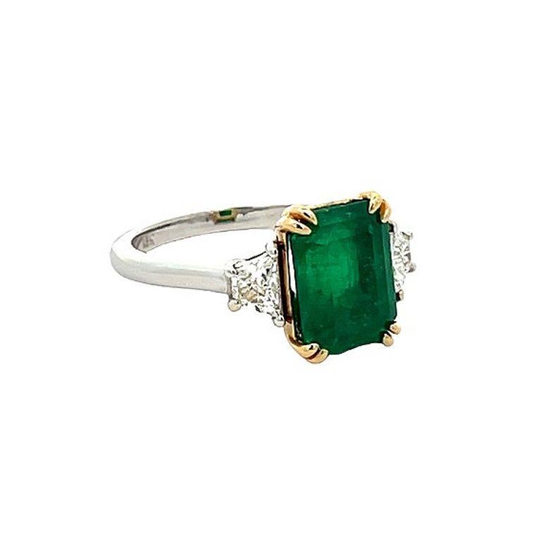 This stunning three-stone ring is sure to take your breath away. The centerpiece boasts a beautiful green emerald of radiant shape from Colombia, considered the best color for emeralds. The emerald is 3.77 carats, flanked by two exquisite trap