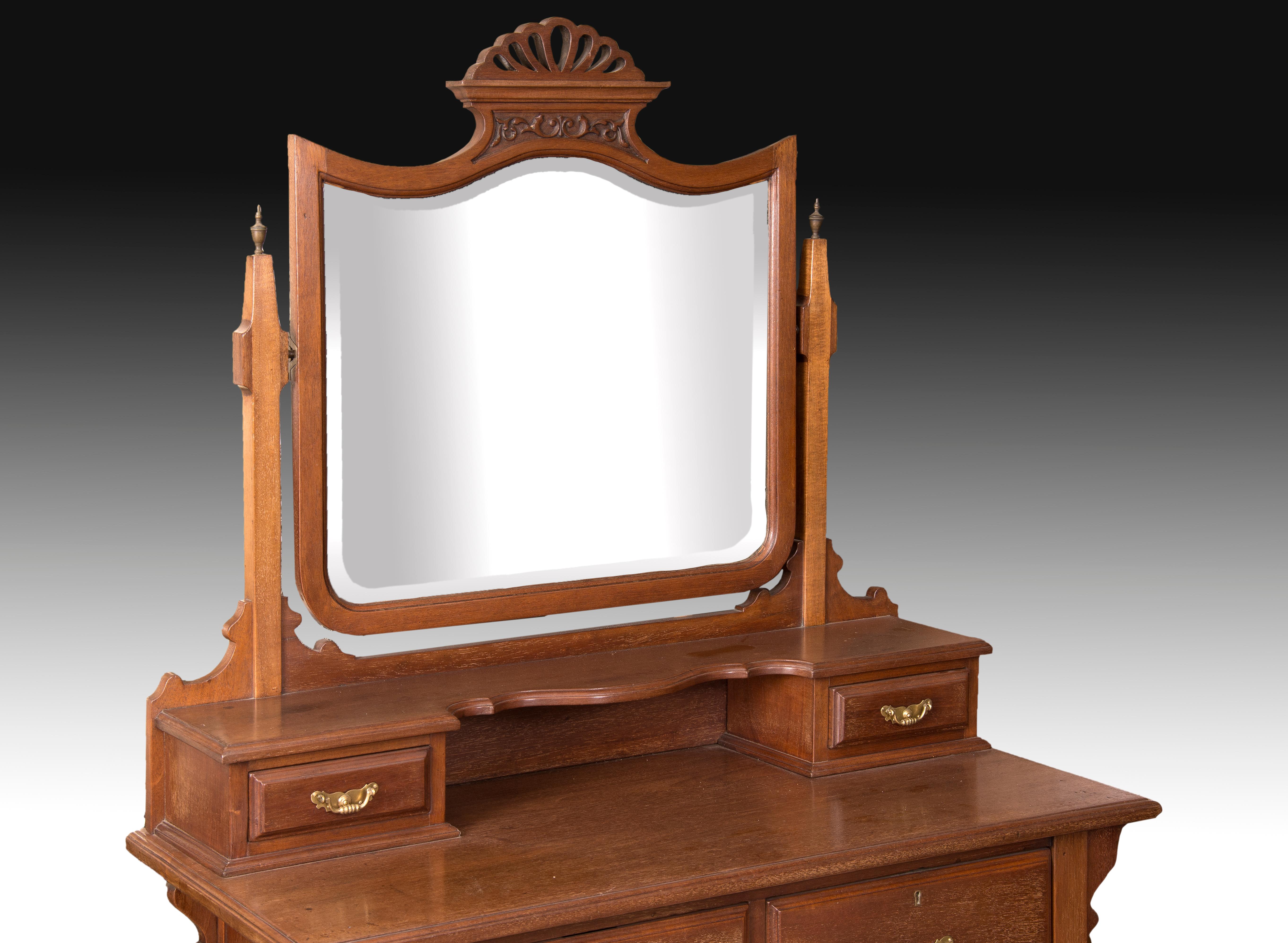 Dresser in carved mahogany wood with metal sheaves on the legs, three drawers to the front and a top board with two drawers flanking a space, and a swing mirror topped with an openwork crest. The few carvings that the furniture presents, its lines