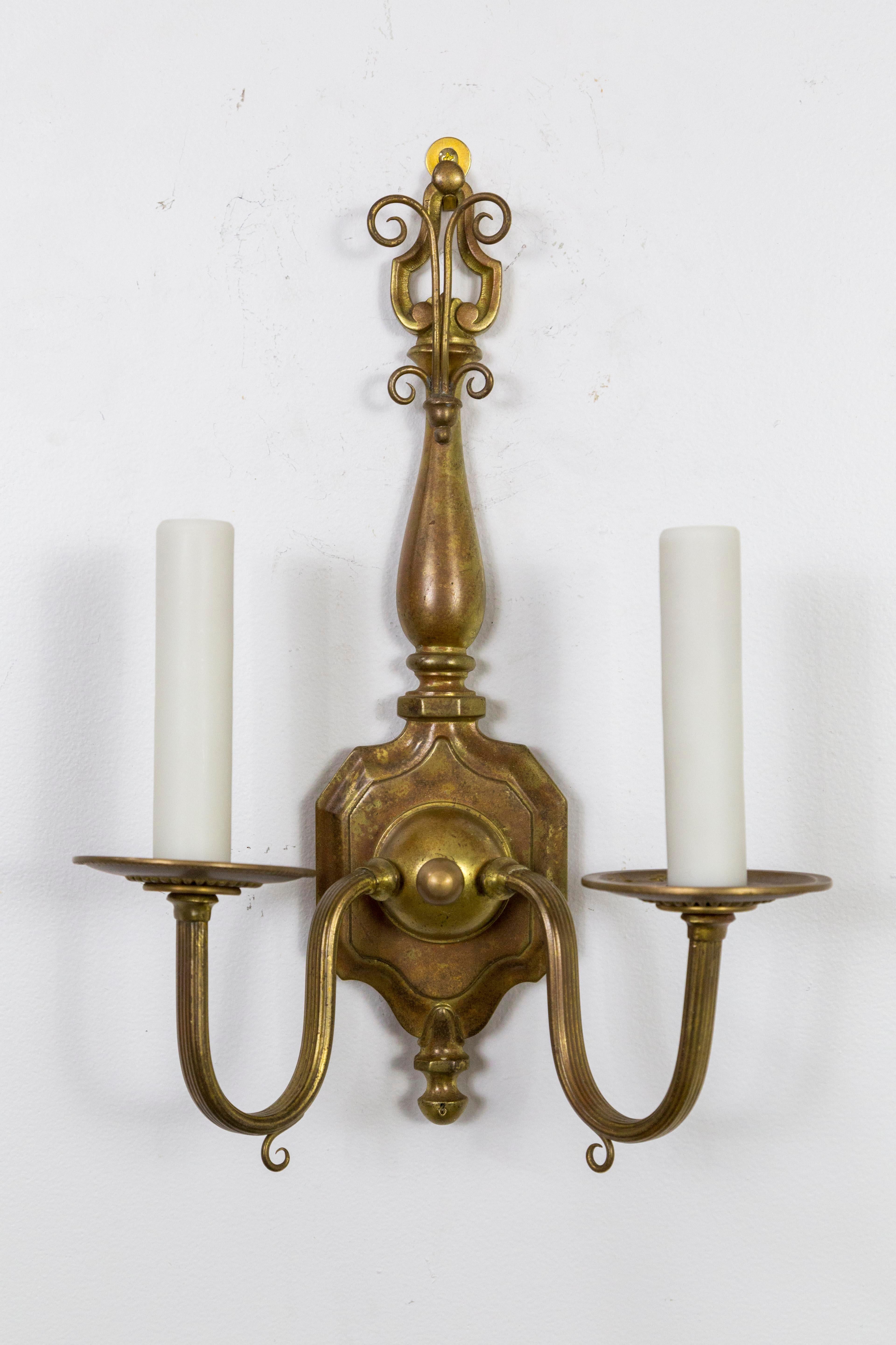 Set of two colonial revival, 2-arm brass sconces. A strong form with simple arms. They originally had crystal decorations, now streamlined with delicate hook accents. American, 1920s. Newly rewired with poly-beeswax candle covers. Measures: 15.75