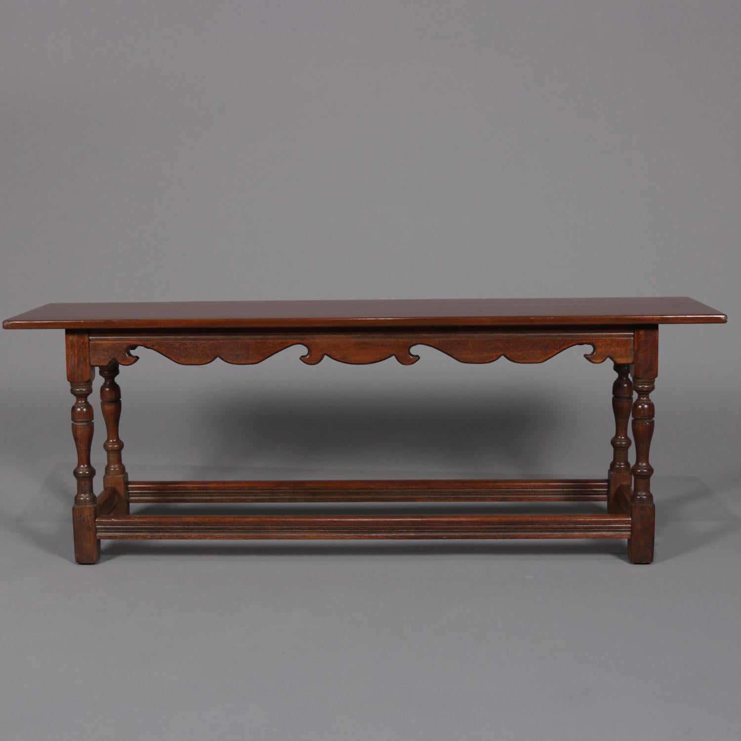 A Colonial Revival Kittinger School long bench features cherry construction with seat surmounting scroll and scalloped apron and raided on turned legs with pegged joints at apron and stretchers, circa 1930

Measures: 18.75