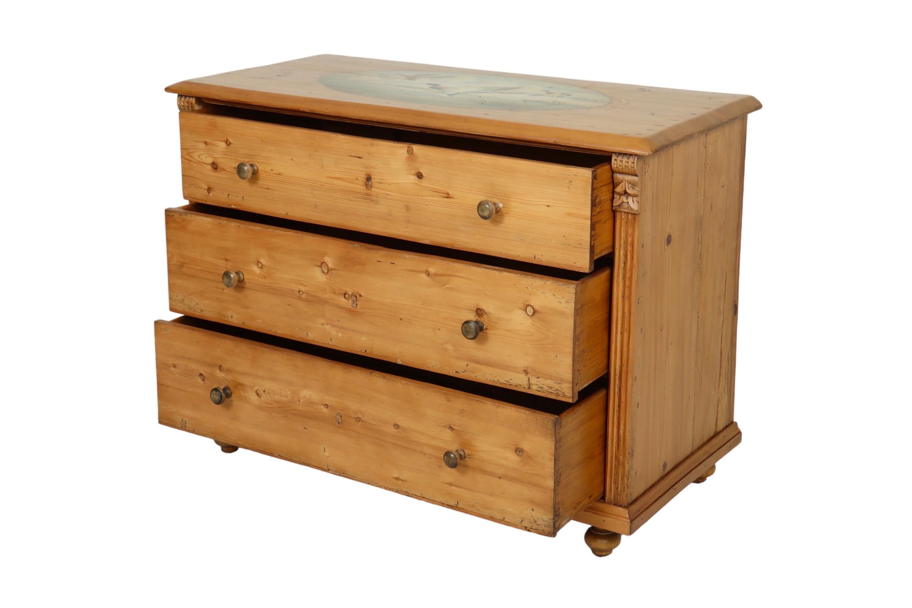 A colonial style dresser made of knotty pine. The dresser is hand painted on top with an idyllic oval scene of four mallard ducks landing on a lake with cattails beneath a fair weather sky. Fluted columns at each side, topped with simply carved