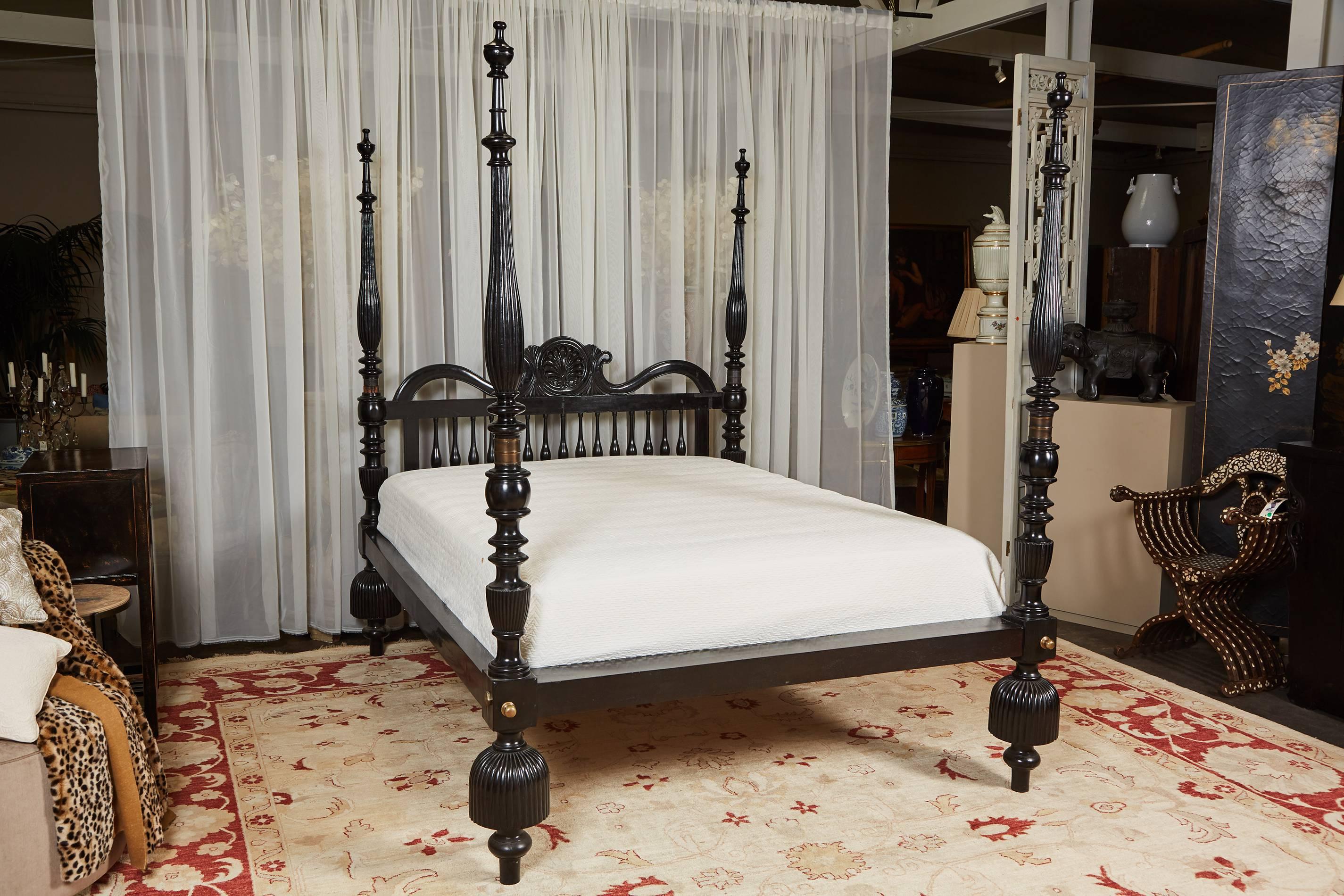 Ein Queen-Size-4-Himmelbett aus Jak-Holz mit ebonisierter Oberfläche. Das Bett verfügt über handgeschnitzte Details, übergroße Füße im Quastenstil und ein Kopfteil mit Muscheldekoration in der Mitte. Zusammengebaut mit gegossenen Messingbeschlägen.