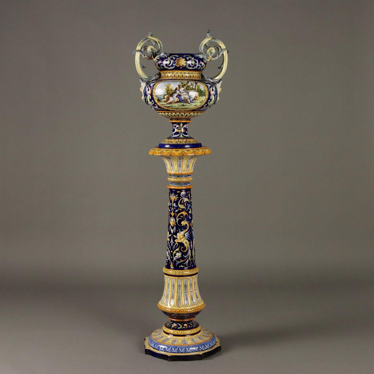 Column with majolica vase with grotesque decorations in shades of yellow, ochre, green, light blue on cobalt blue background. The vase has two side handles in the shape of masks and plant motifs. On the belly of the vase painted inside reserve,