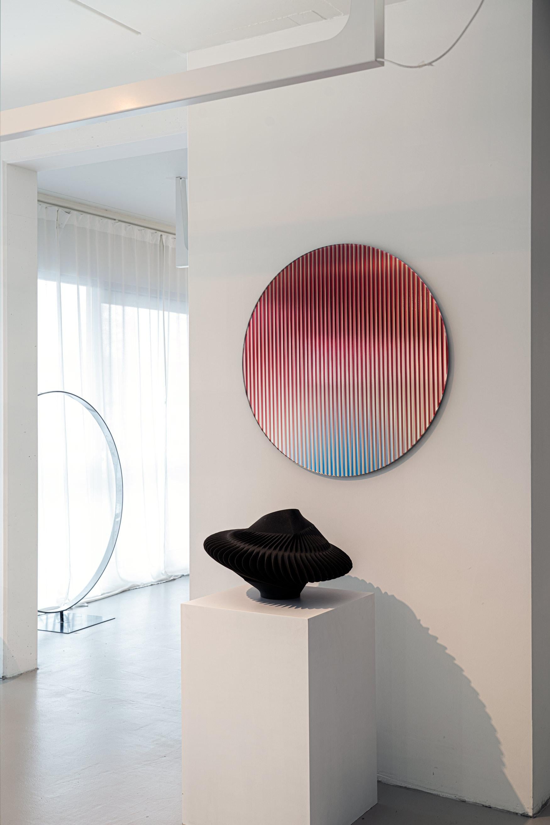 Die spiegelnde, farbige, gewellte Glasplatte, die eine Farbpalette in den Raum bringen soll, reflektiert das Licht im Raum und sorgt für Bewegung und Farbe, während sie abstrakte Spiegelungen erzeugt. Das Werk streut das Licht durch seine gewellte