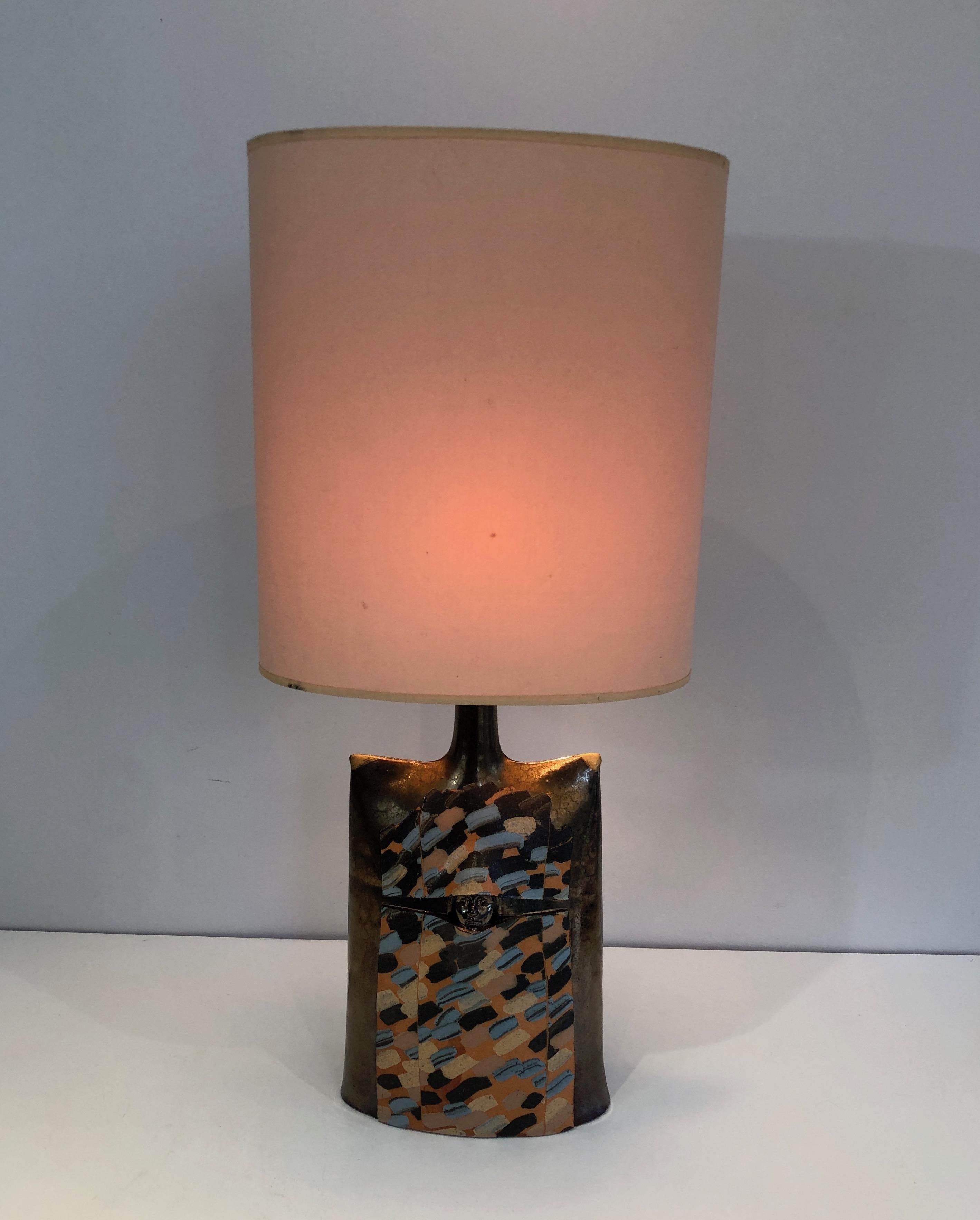 This colored table lamp is made of ceramic with a face in relief. This is a French work, circa 1970.