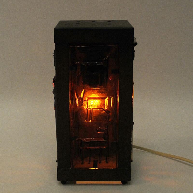 Lovely rectangular table lamp of glass and copper by Erik Höglund, Sweden, 1960s. A glass table lamp with four decorated amber brown glass panels (Kosta Boda) of people and animals in which gives a beautiful red light when lit. Brown copper frames