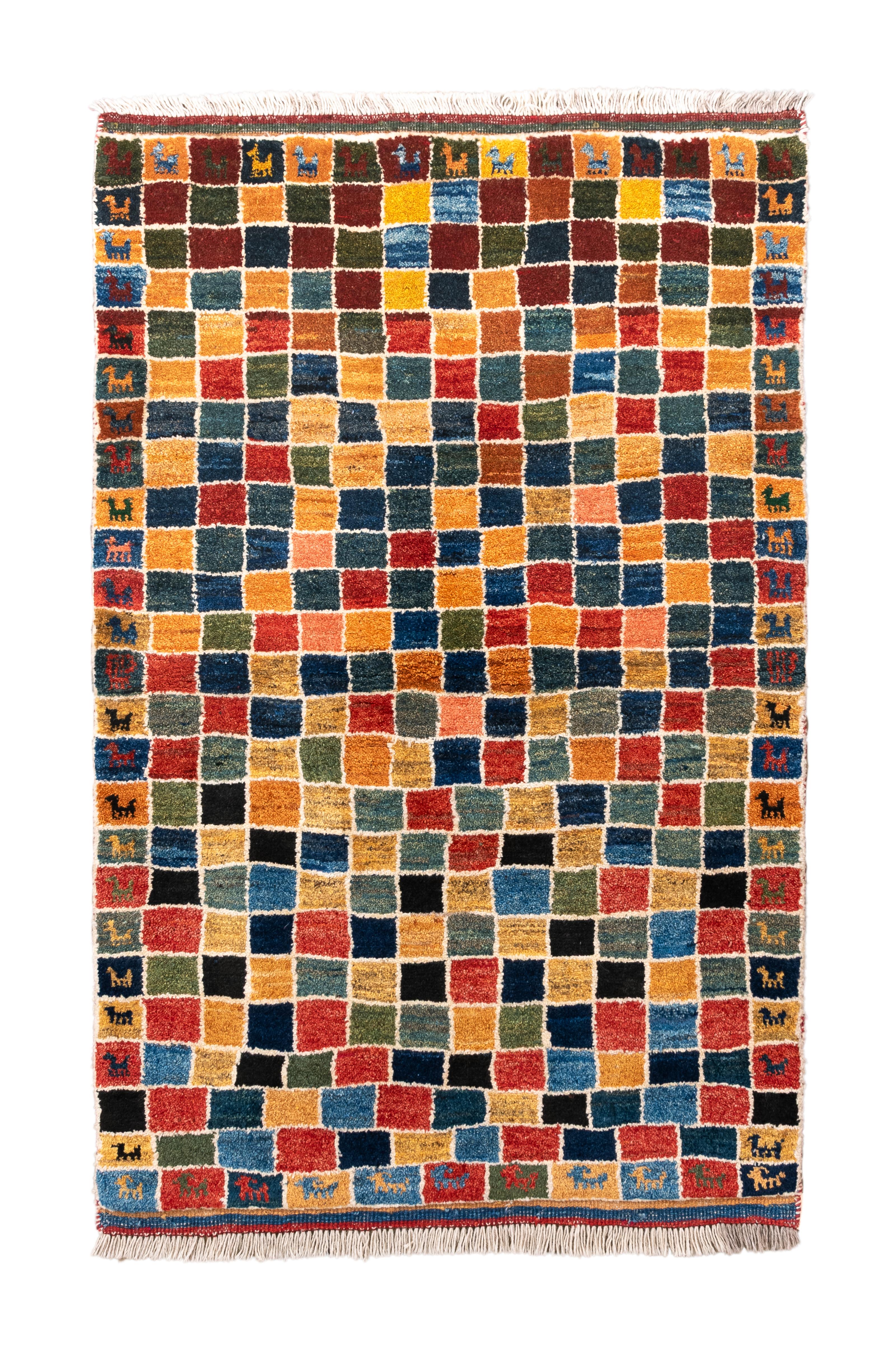  A mesmerizing Gabbeh rug woven in a radiant patchwork of jewel-toned squares, framed by a charming border of stylized animal motifs. Each small square, slightly irregular and organically colored, creates a dynamic visual rhythm while maintaining an