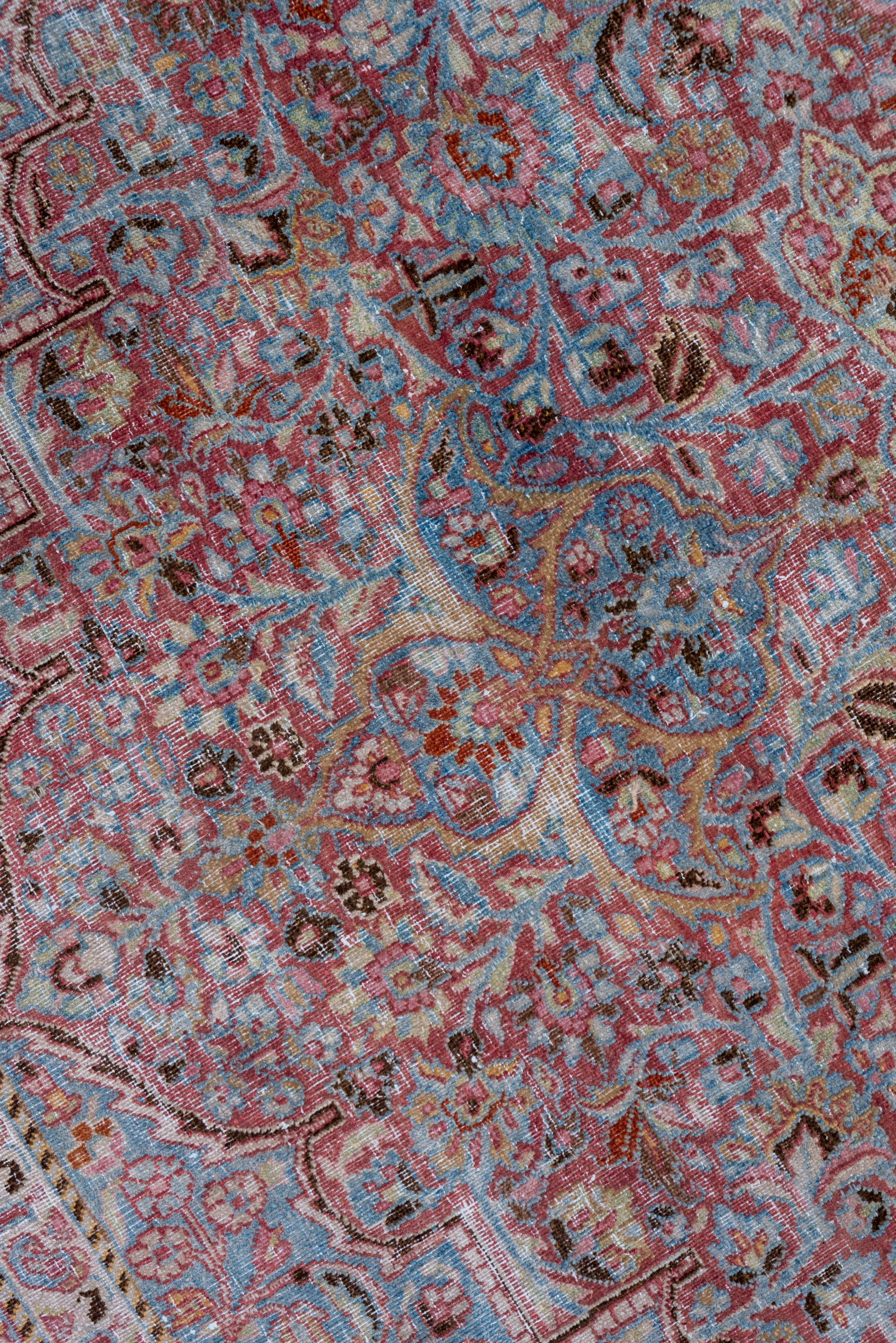 This now-distressed NE Persian city carpet show pale blue leaf and flower corners, positioning a coral field around an arabesque-defined lappeted light blue medallion with a rust sub-medallion. Rust main border with inward and slanted petal