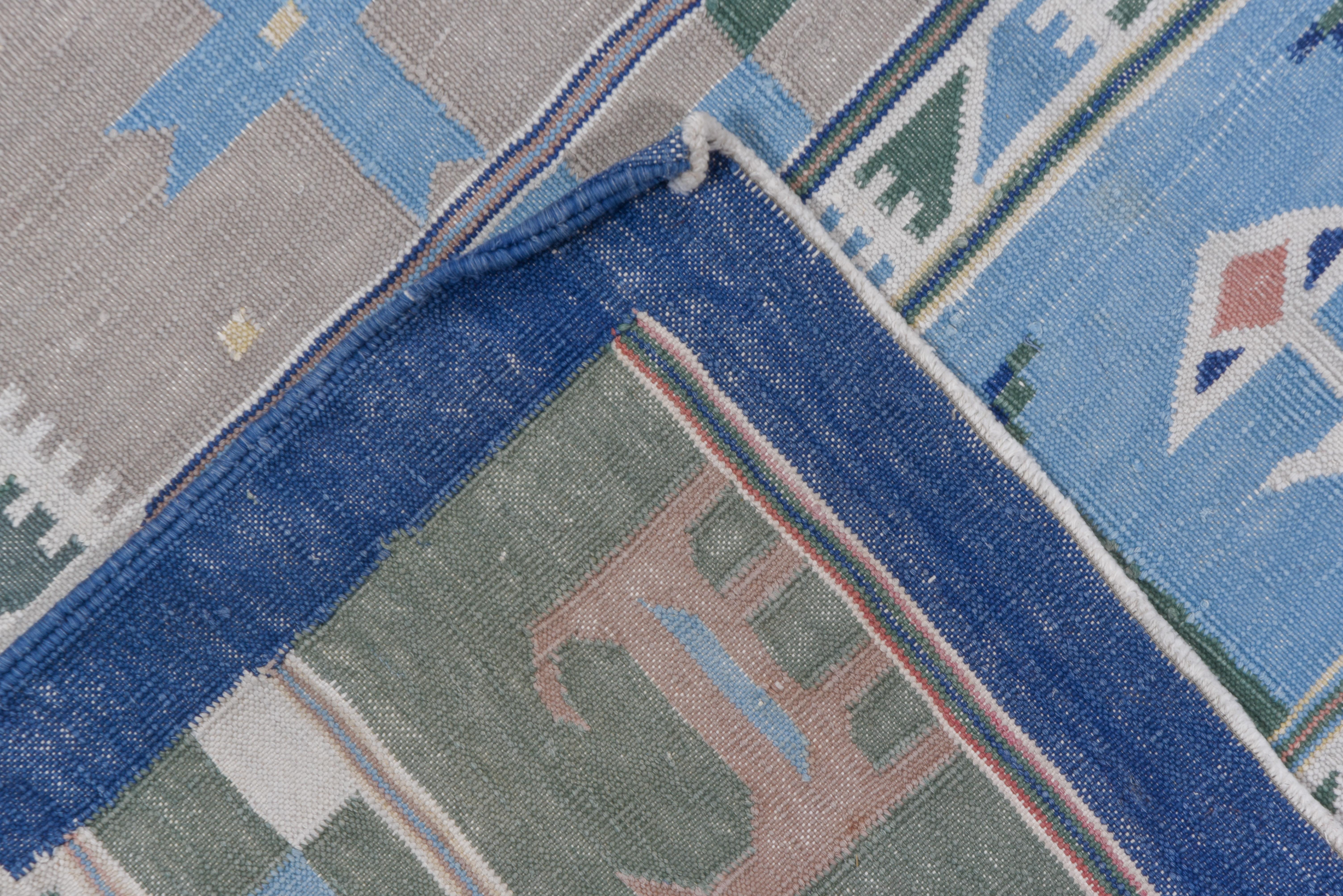 Das gemusterte Feld dieses Baumwoll-Flachgewebes zeigt horizontale Streifen mit stilisierten Vögeln, Chevrons, Kreuzen und breiten Zickzacklinien, meist in Blautönen. Blassblaue Hauptbordüre mit Tieren, Vögeln, Blumen und Kreuzen. Zusätzliche