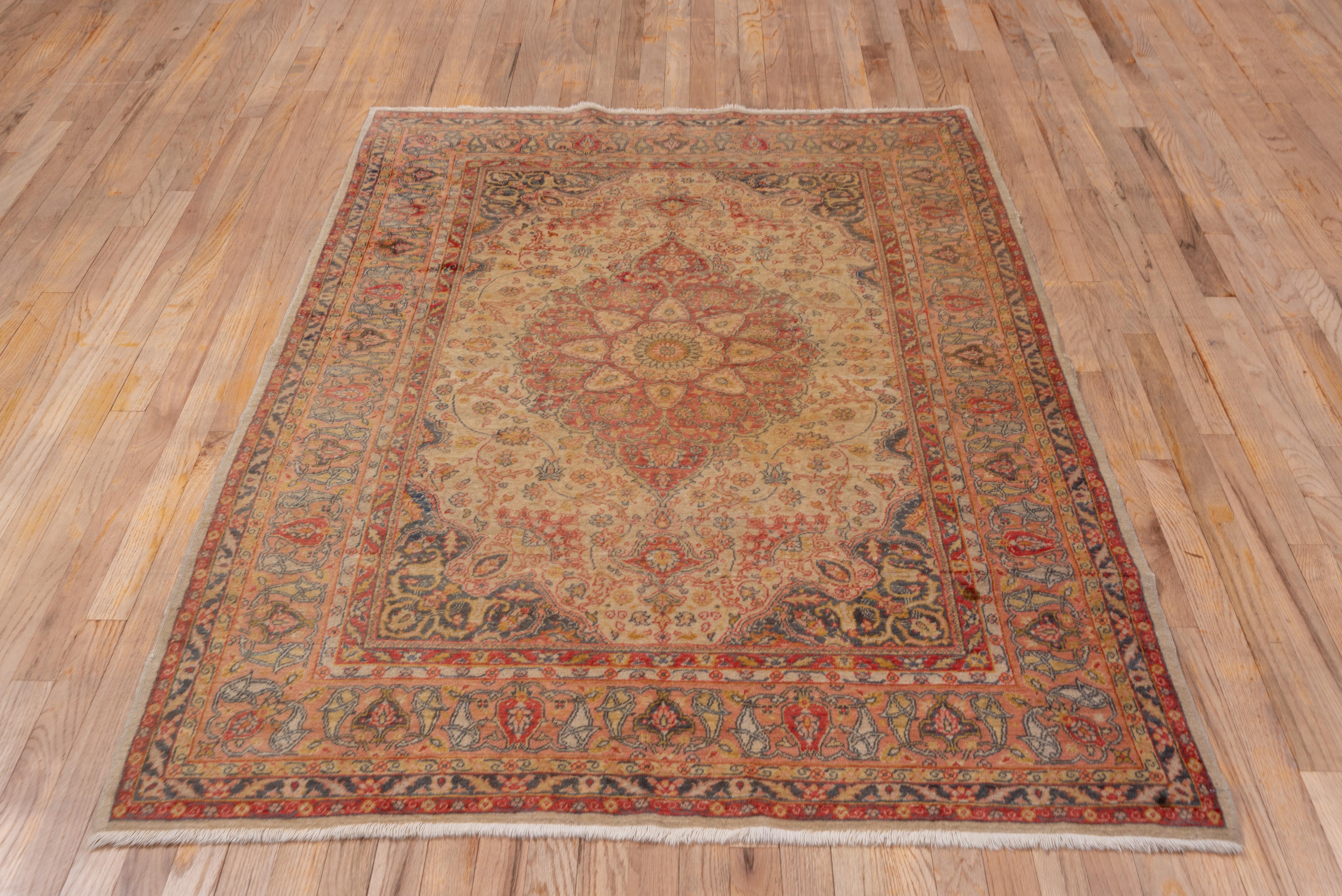 In the Tabriz tradition and softly colored, the sandy-straw field displays a tall, pendanted abrashed brown medallion with an eight point straw sub-medallion. Light slate blue corners with trumpet volute arabesques. Straw-beige border with shield