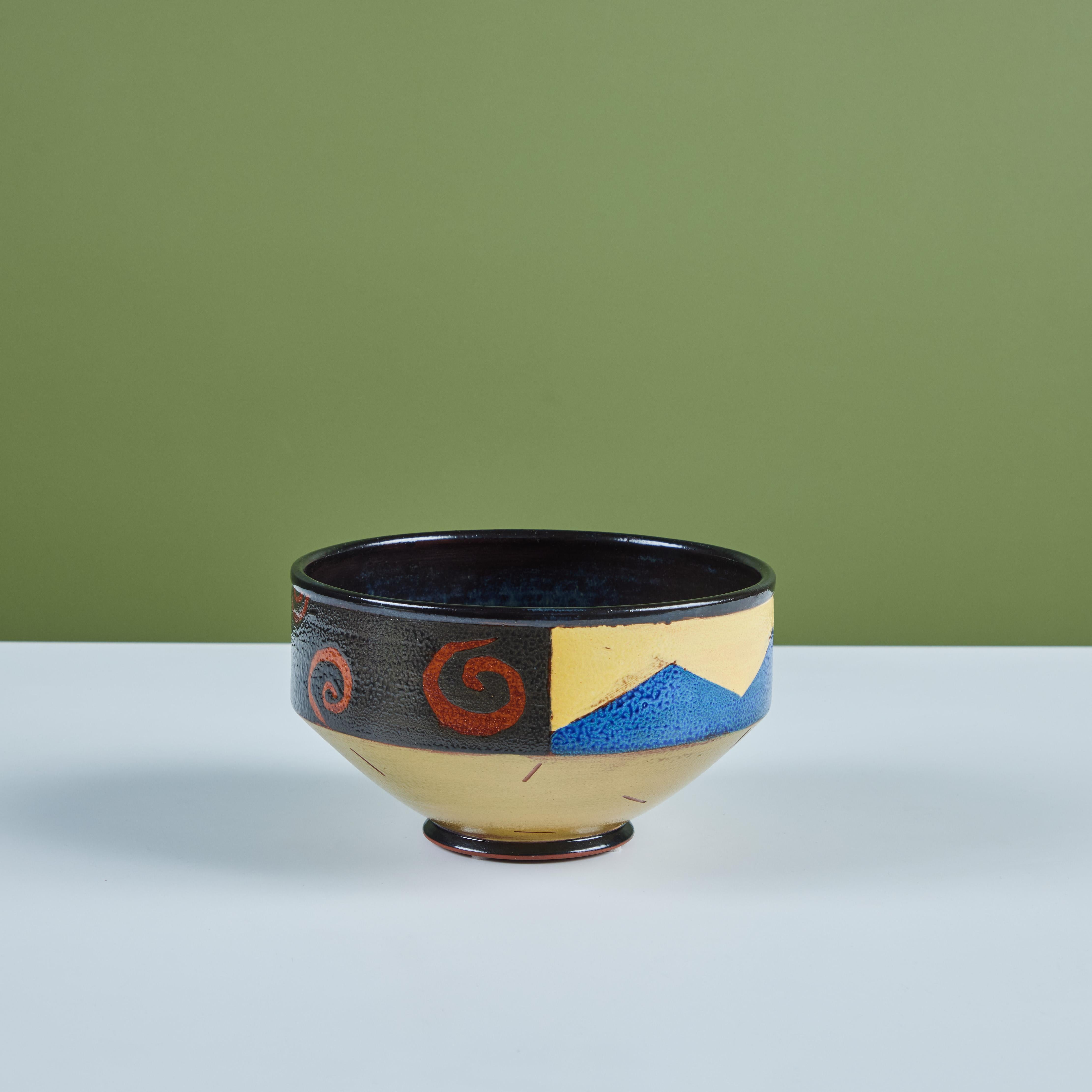 Ceramic bowl signed by the artist. The playful bowl has a black glazed interior. The exterior showcases different designs, geometric blue and yellow triangles, bright blue and orange leaves and burnt orange swirls. The bowl tapers towards the bottom