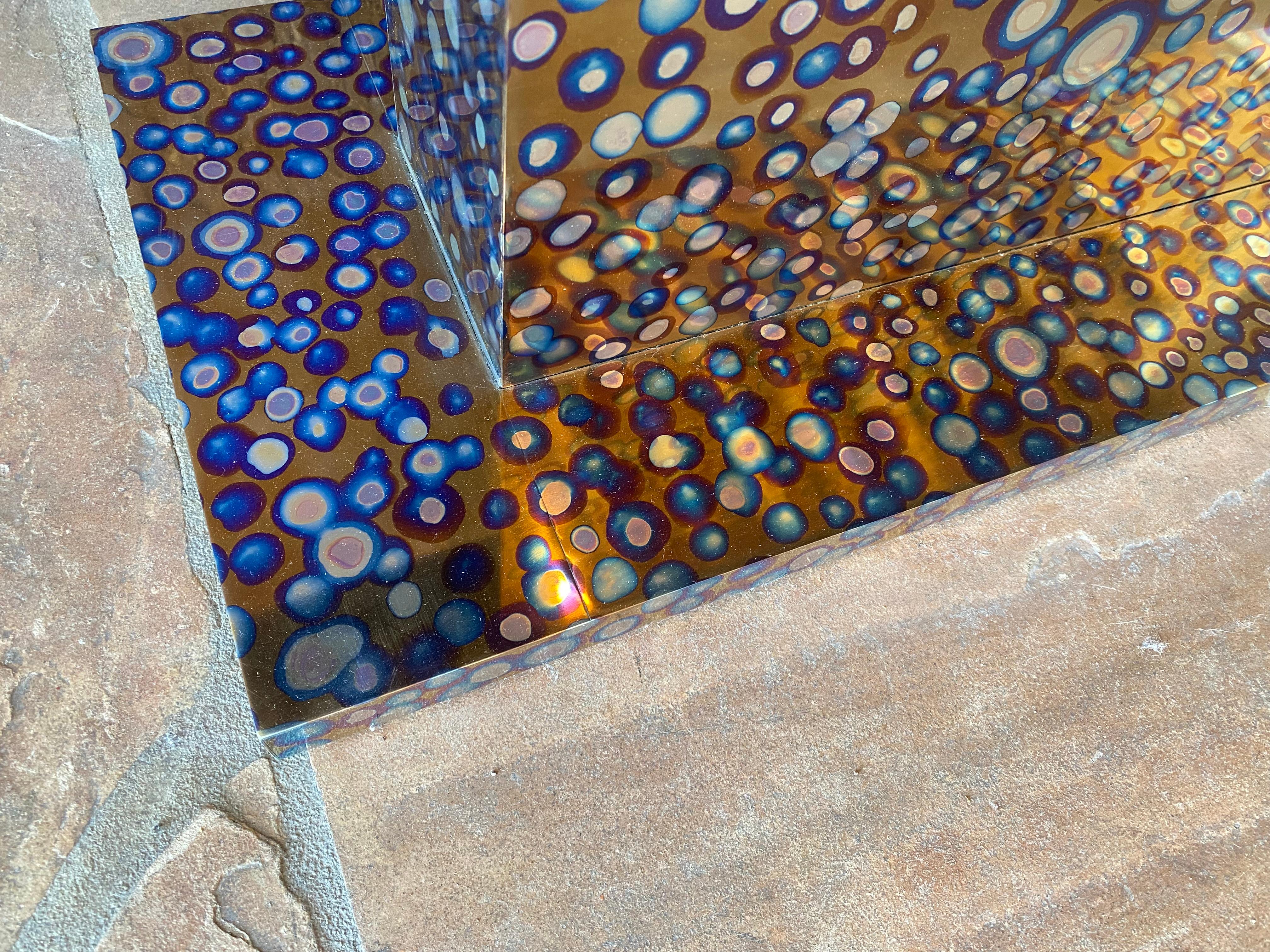 This console made of patinated titanium and signed by Xavier Mennessier features a parallel rectangular base and top, connected by a solid block designed in a shiny, rounded pattern reminiscent of colorful bubbles of life. The piece is covered with