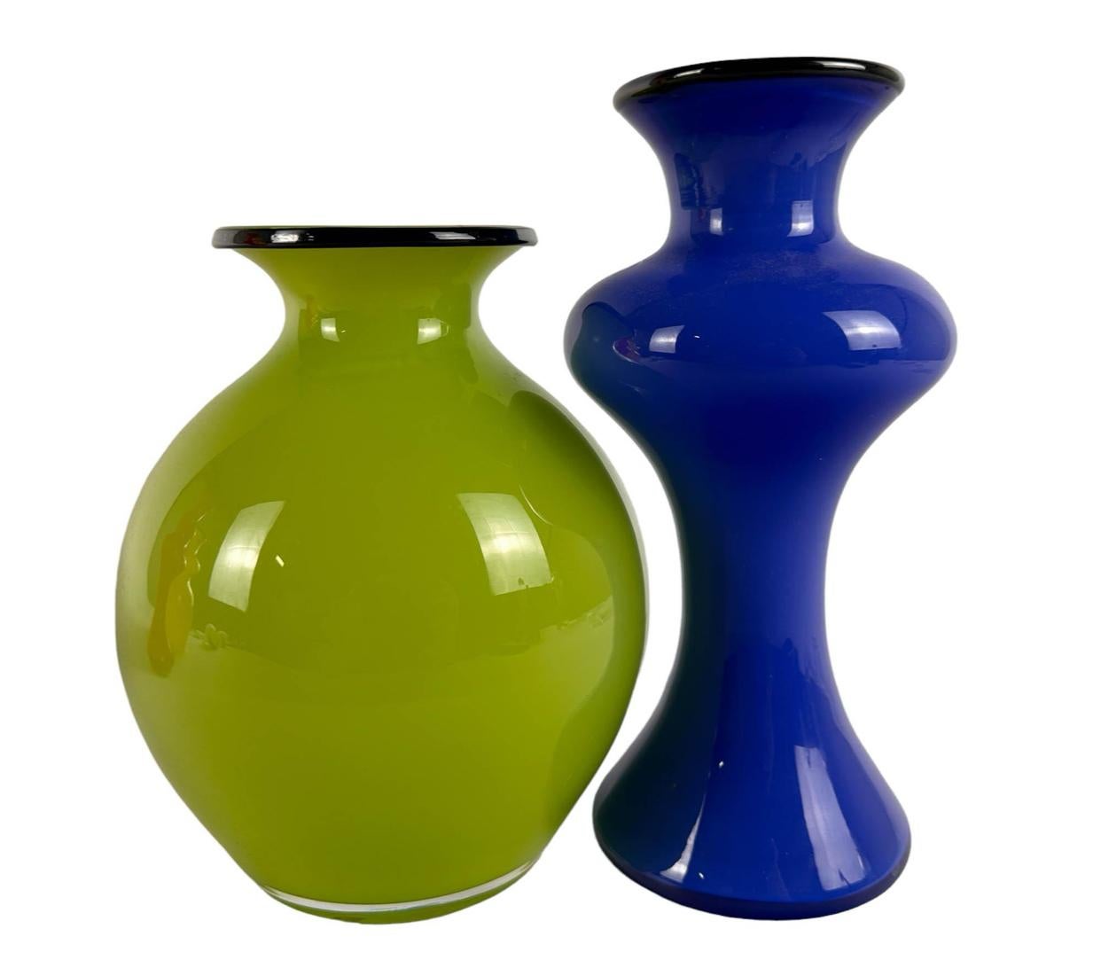 A collection of four vintage art glass decanters by Swedish Design Studio Strombergshyttan. Colors include; bold yellow glass, green, blue and red, each having a black glass ring around the top lip. Their are only two stoppers, which feature a