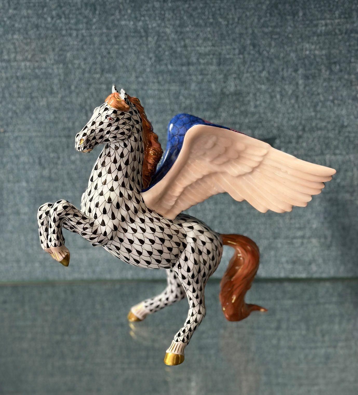 Colorata figura in porcellana dipinta a mano che raffigura un pegaso in piedi ornato dall'iconico disegno a squame di pesce in bianco e nero. Le sue ali sono multicolore e il pezzo include anche delicati dettagli in oro. Marchio Herend Hungary sulla