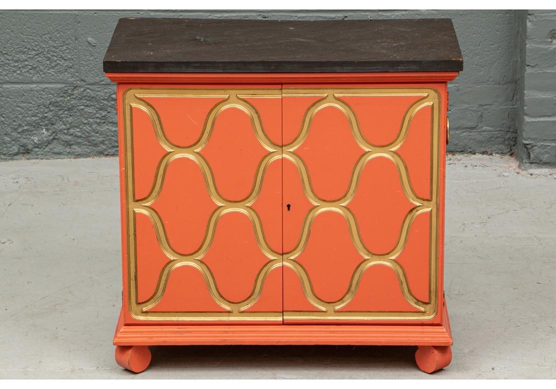 Dorothy Draper Espana Cabinet in coral with gilt accents. A colorful and highly decorative painted and gilt chest in the Hollywood Regency style. Hollywood Regency style small chest in a high gloss Coral and Gilt finish. A double door chest in coral